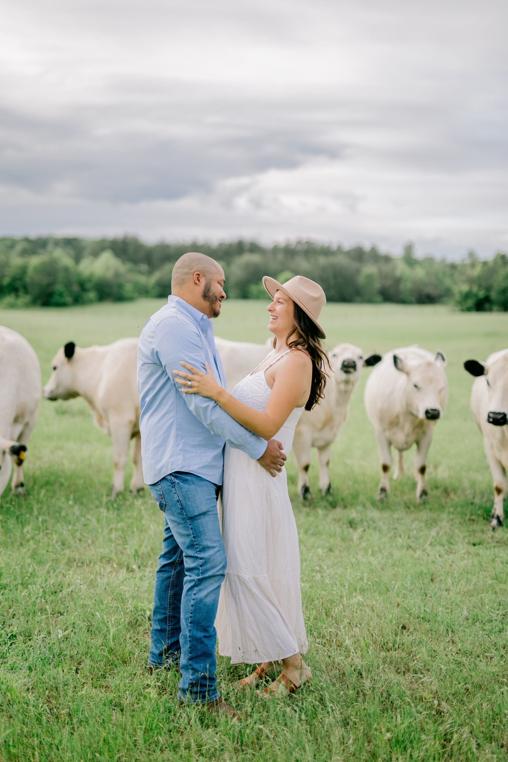 the bride and groom pose in front of cows at their farm engagement session
