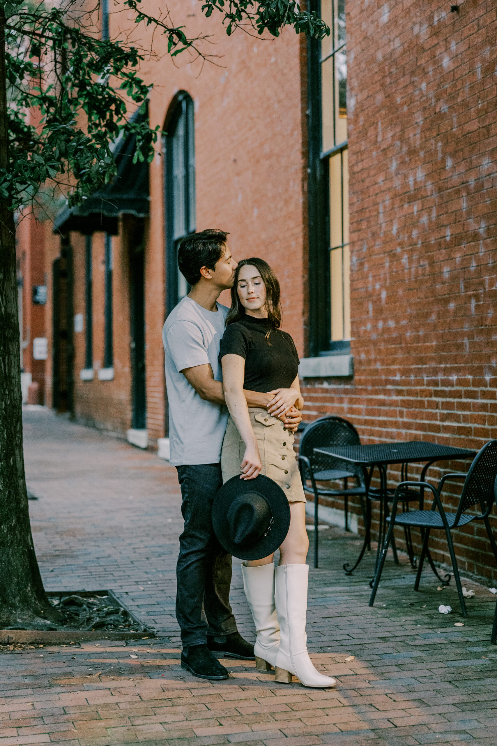 Man hugging woman from behind as woman's eyes are closed on a brick walkway