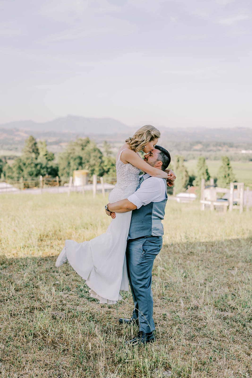 A Sonoma county vineyard wedding photo of the bride and groom as the groom picks the bride up during sunset.
