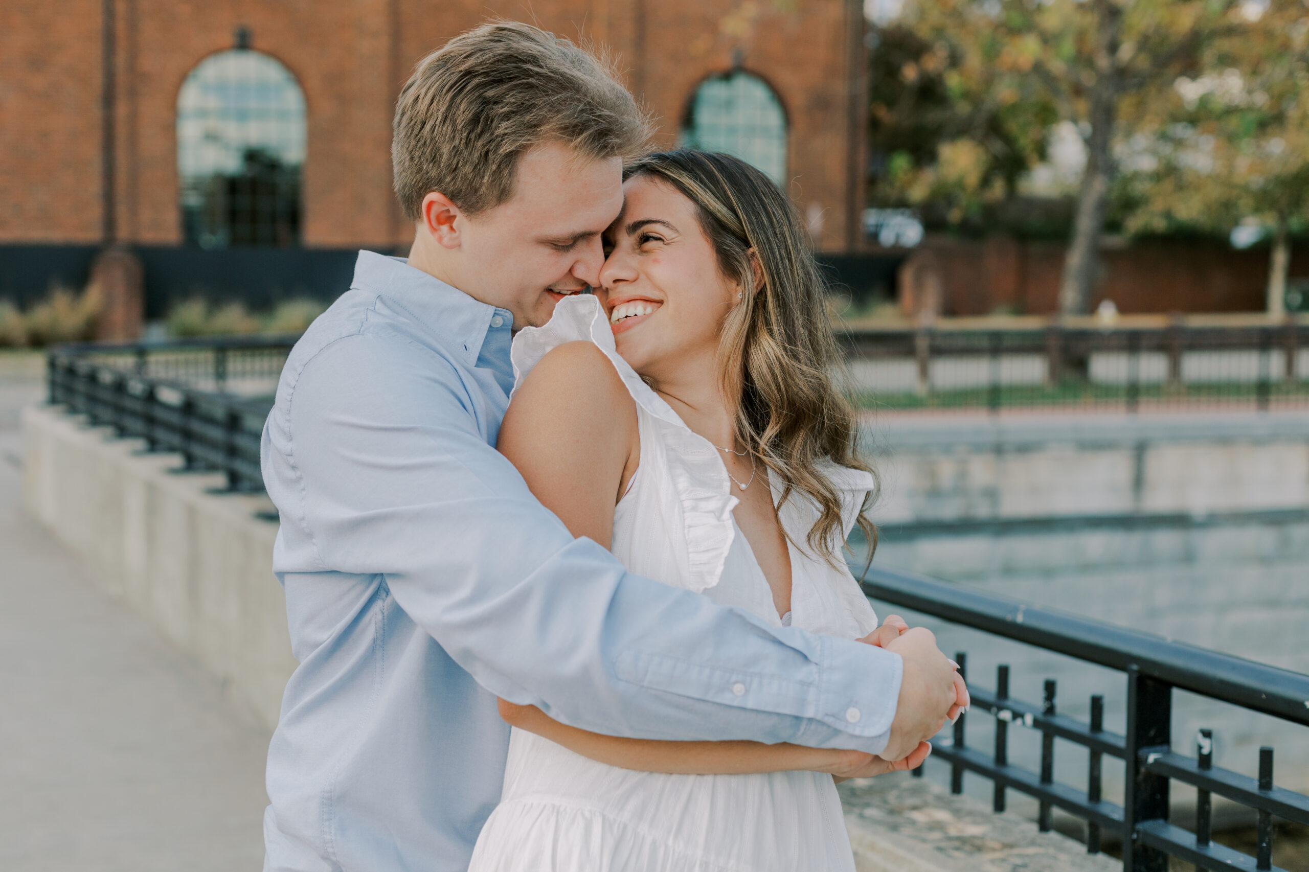 Man hugging woman from behind, she looks back smiling at him, his arms wrapped around her, their hands holding on to one another at their tredegar ironworks fall engagement session