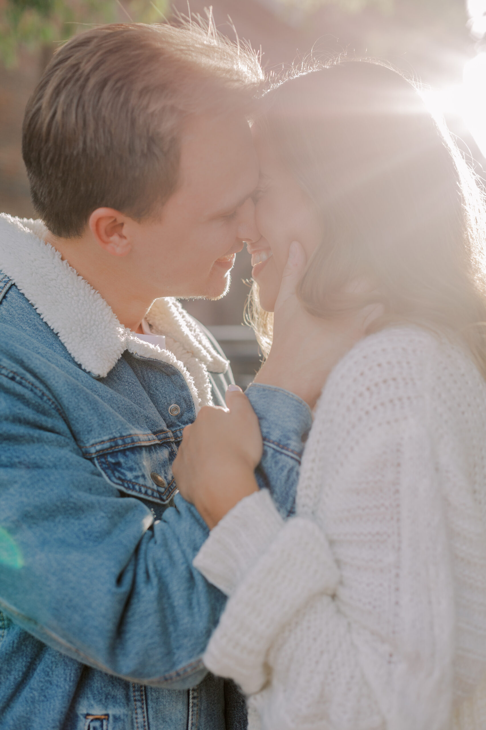 Close up image of couple about to kiss, smiling at one another, as sun beams pour out from corner of photo