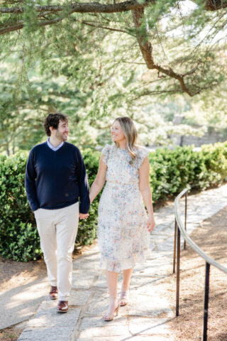 Engaged couple walking at maymont park holding hands smiling at one another