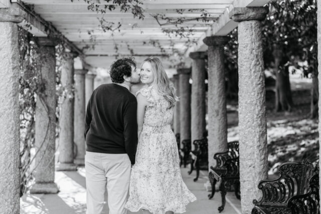 Black and white photo of man kissing woman on her cheek as she smiles back at camera