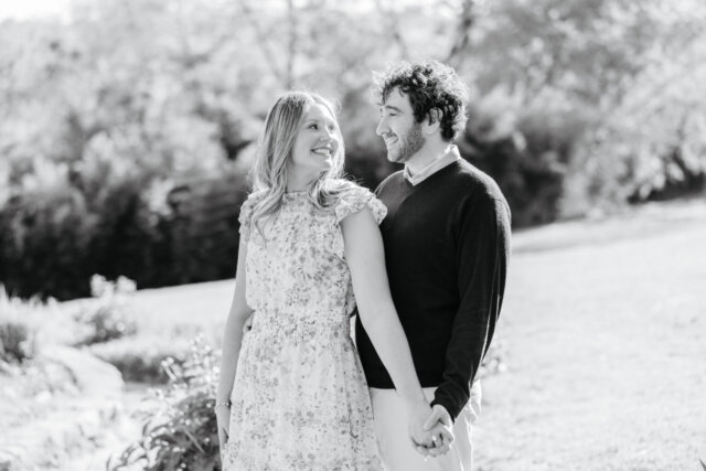 Black and white photo of engaged couple holding hands and smiling at one another at maymont park