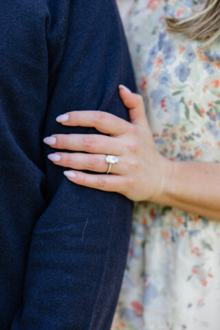 Detail photo of woman's left hand on man's arm to show off her pink nails and diamond engagement ring