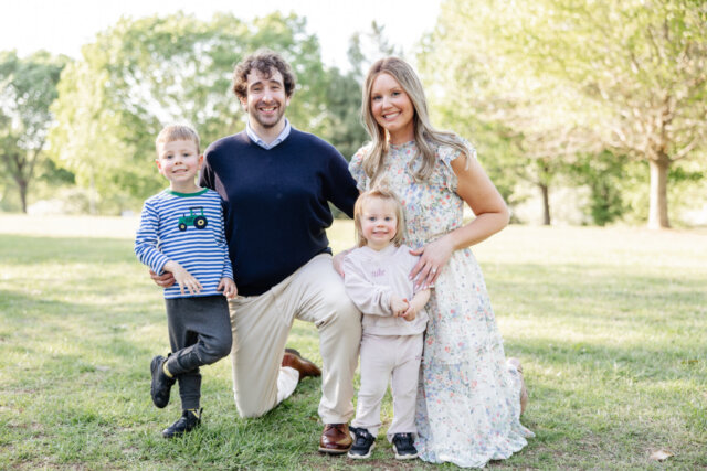 Man and woman stand with two young children all smiling at camera