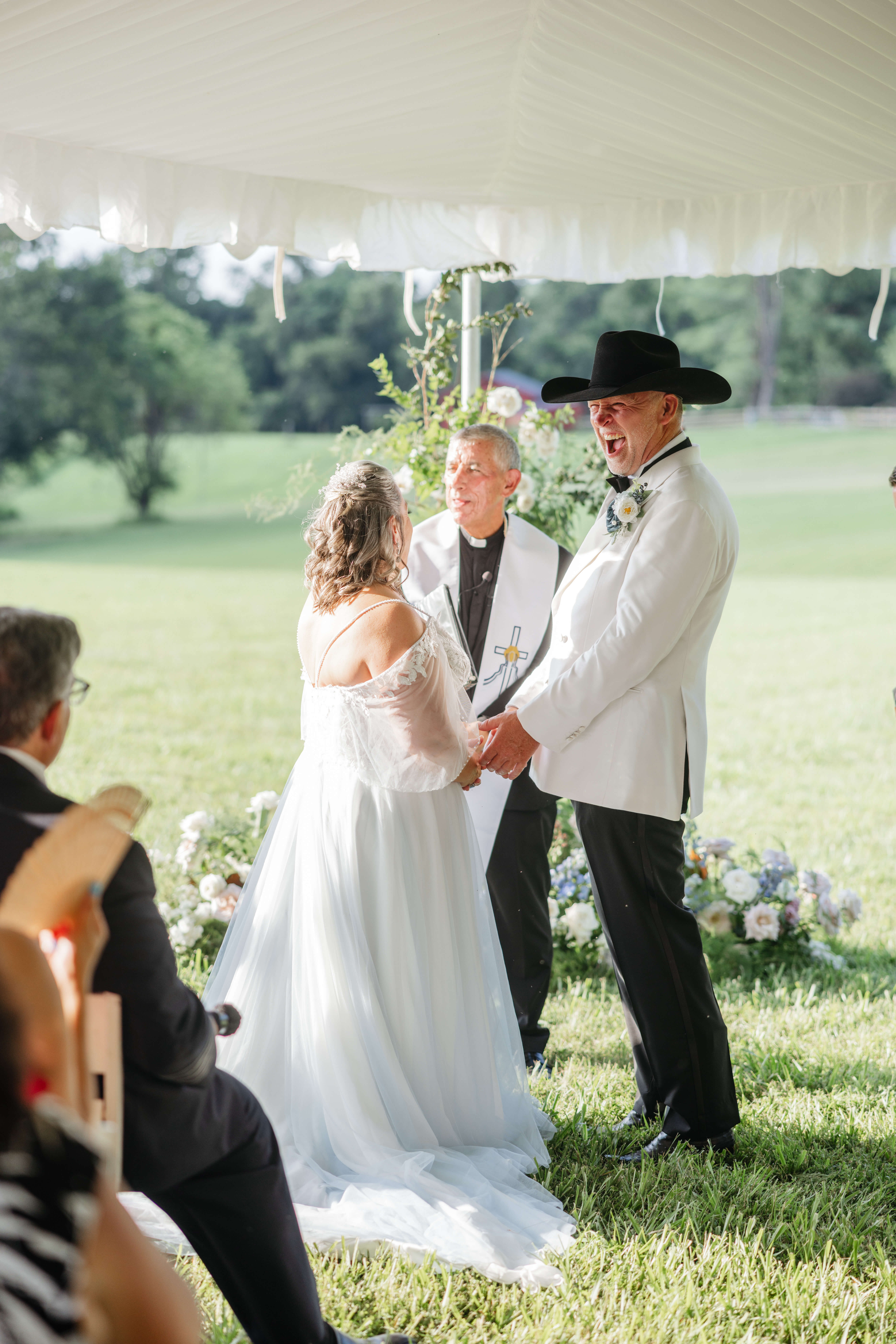 Private Residence Summer Wedding 18 Groom laughing while holding hands with bride during their wedding ceremony