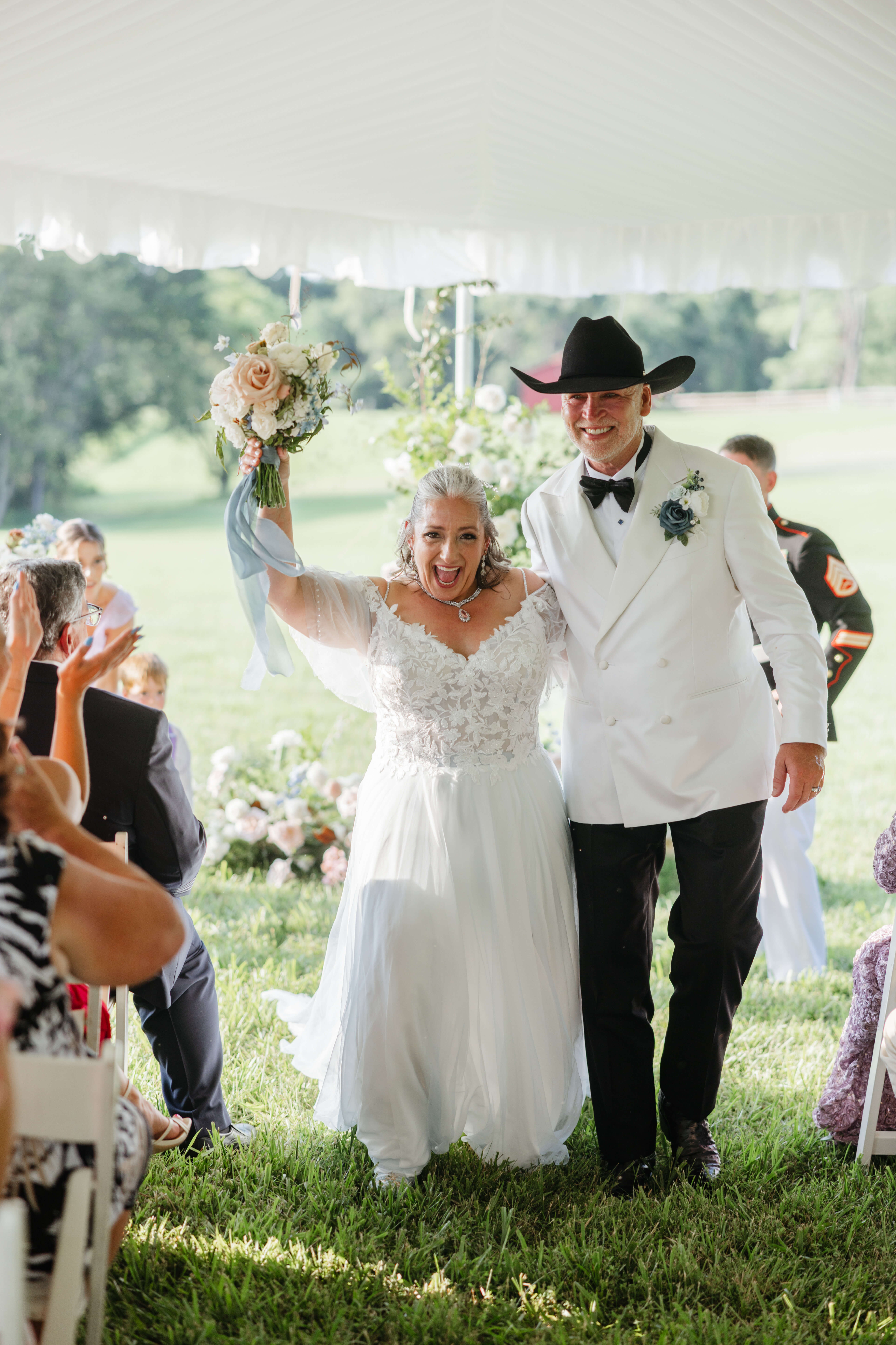 Private Residence Summer Wedding 22 Bride holding her bouquet up in the air in celebration as her and groom walk back up the aisle