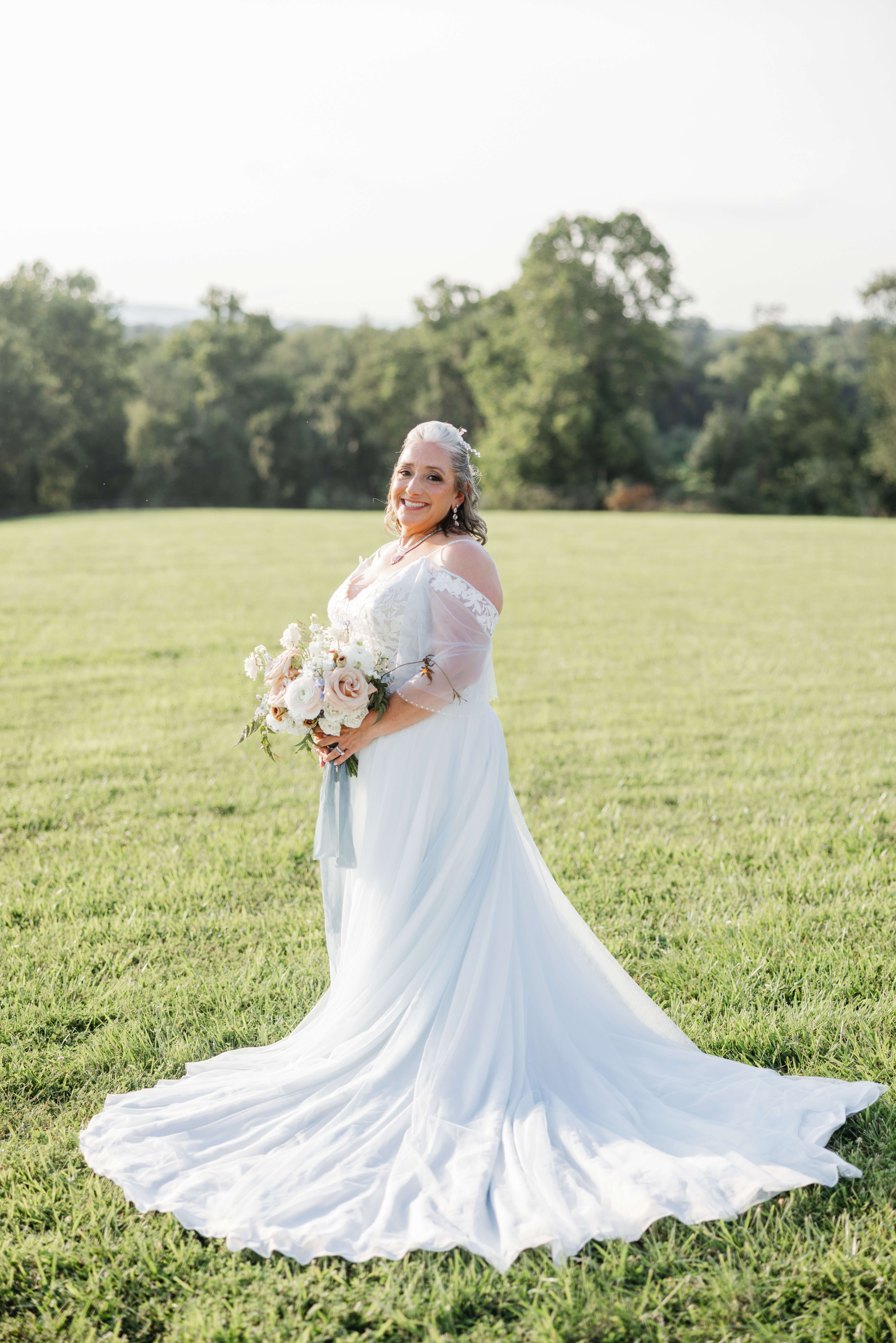 Private Residence Summer Wedding 27 Solo photo of bride with her dress train laid out in front of her, smiling at camera as she holds her bouquet