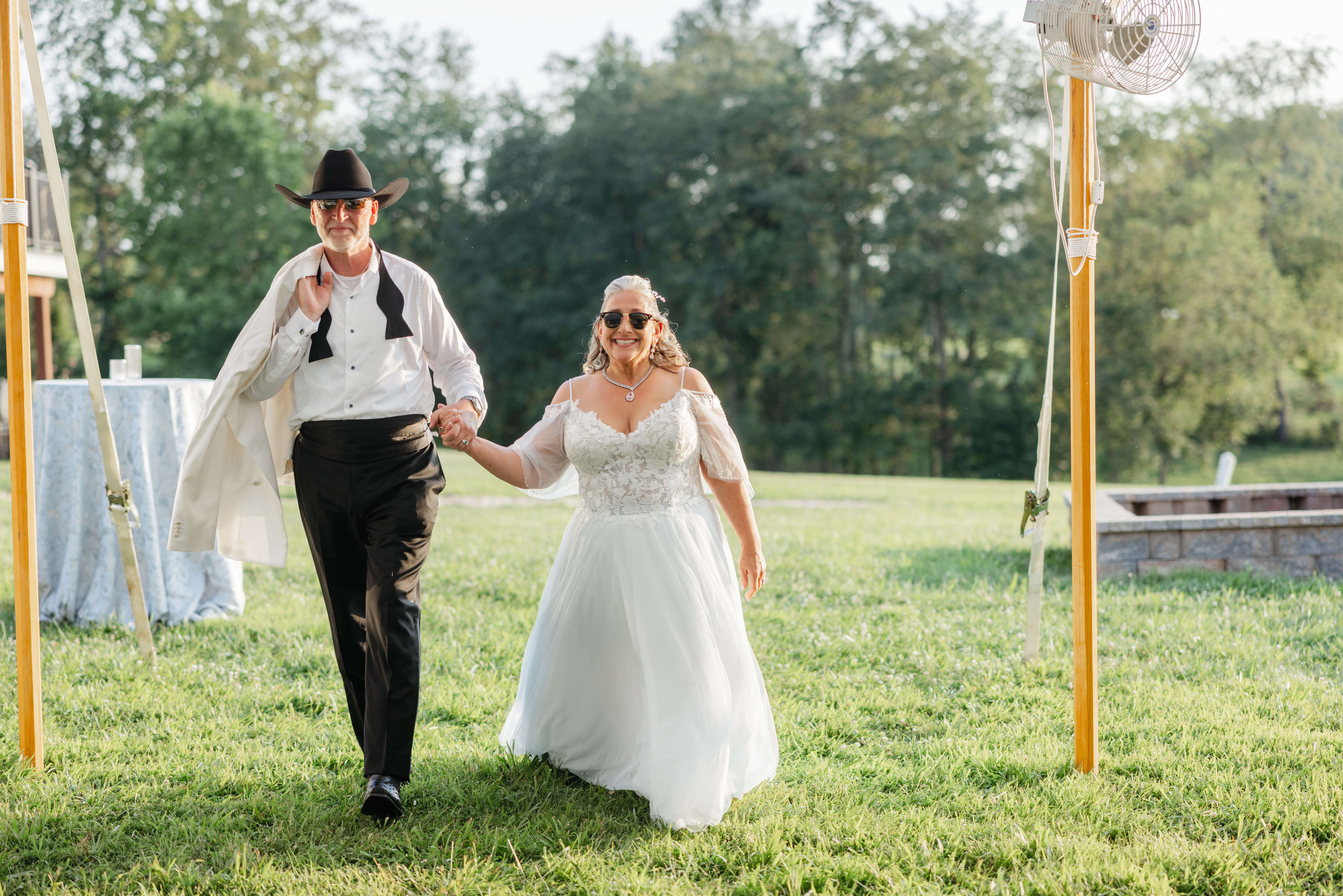 Private Residence Summer Wedding 29 Bride and groom enter their reception with sunglasses on, smiling and holding hands