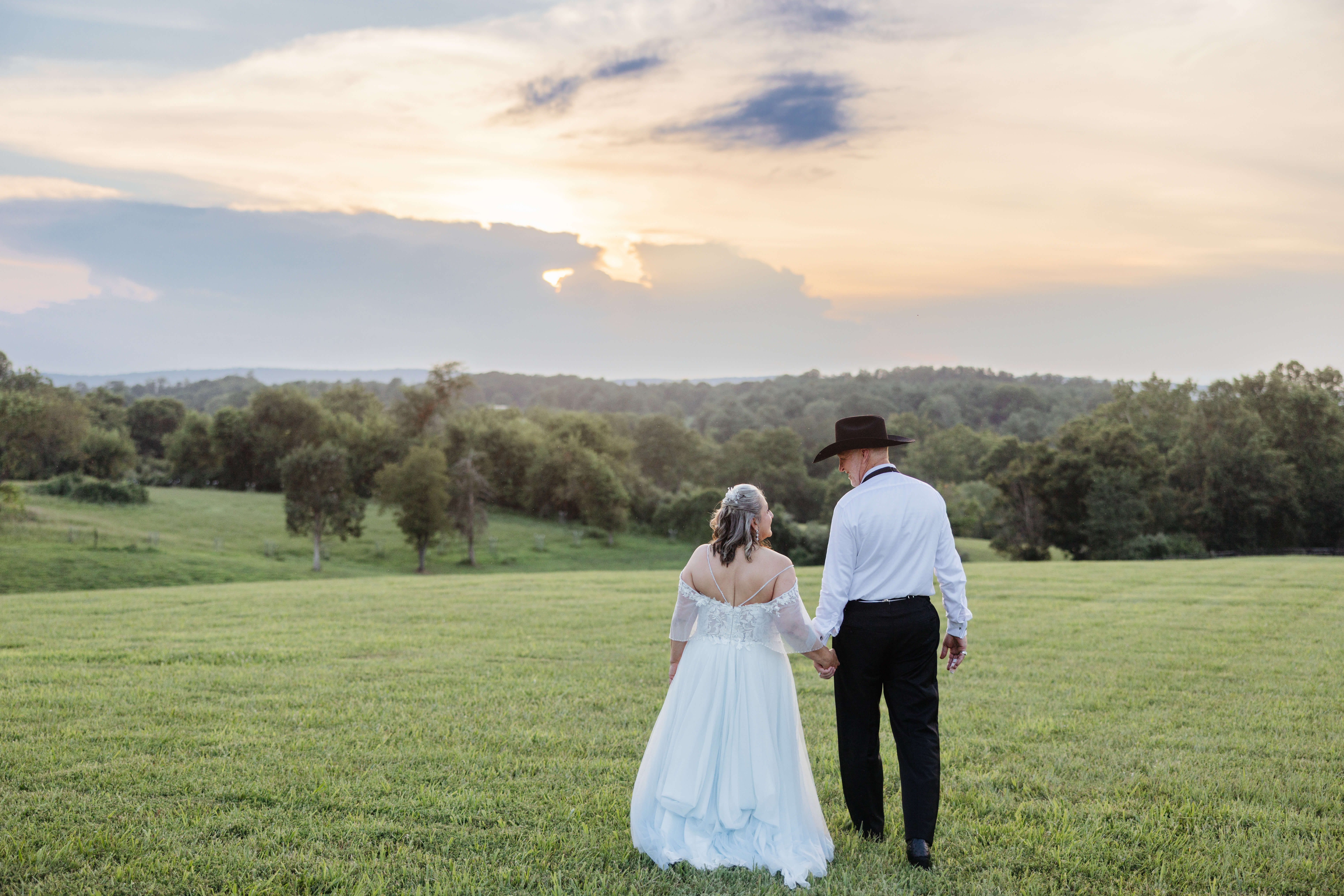 Private Residence Summer Wedding 37 Bride and groom walking hand in hand away from camera towards sunset view and landscape