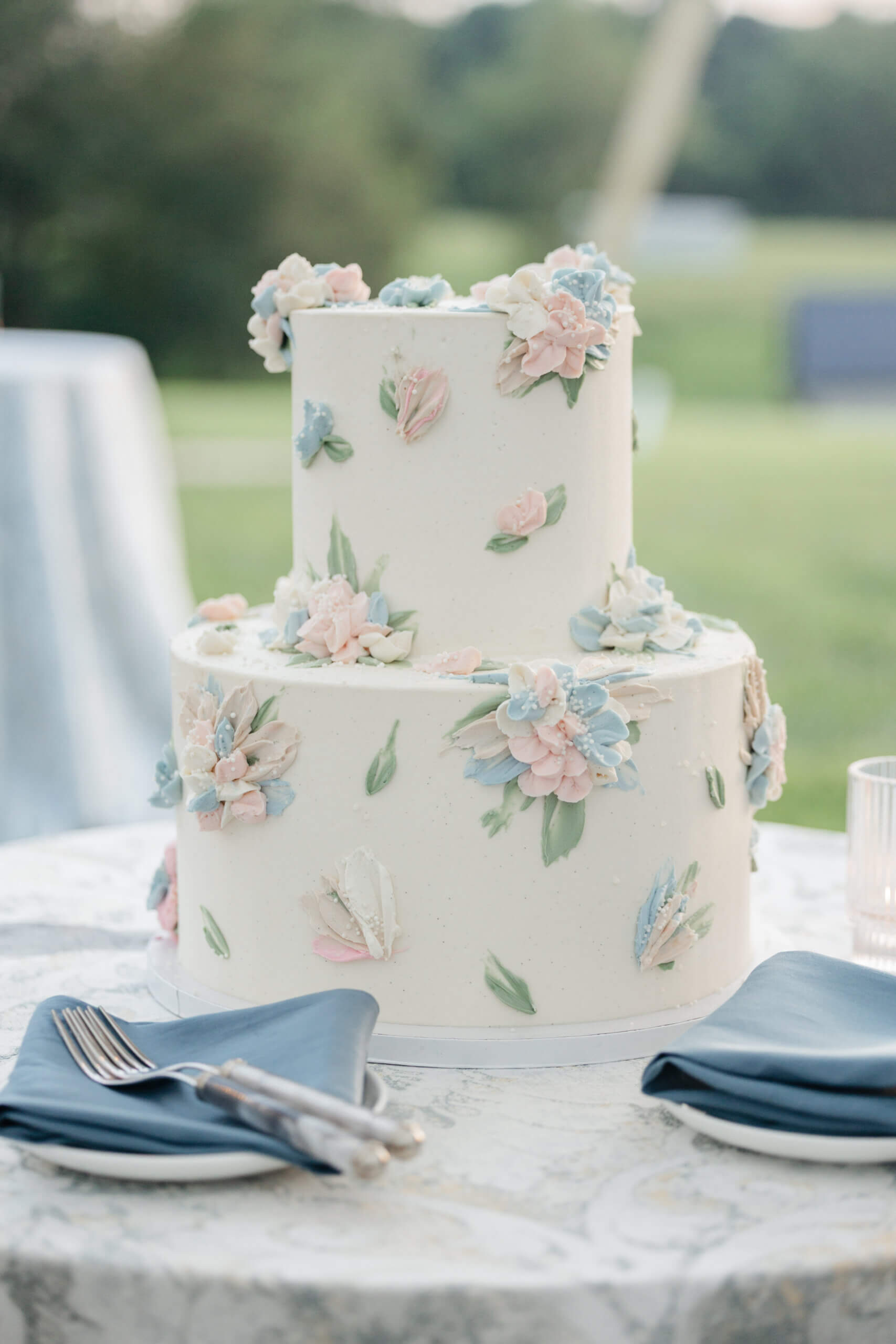 Private Residence Summer Wedding 39 Close up photo of white wedding cake with icing flowers of blue and pink on it