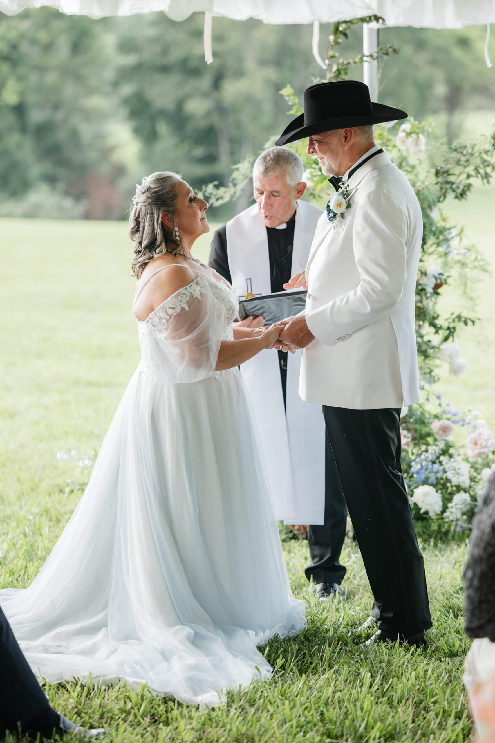 Private Residence Summer Wedding 16 Bride and groom hold hands as officiant reads from book