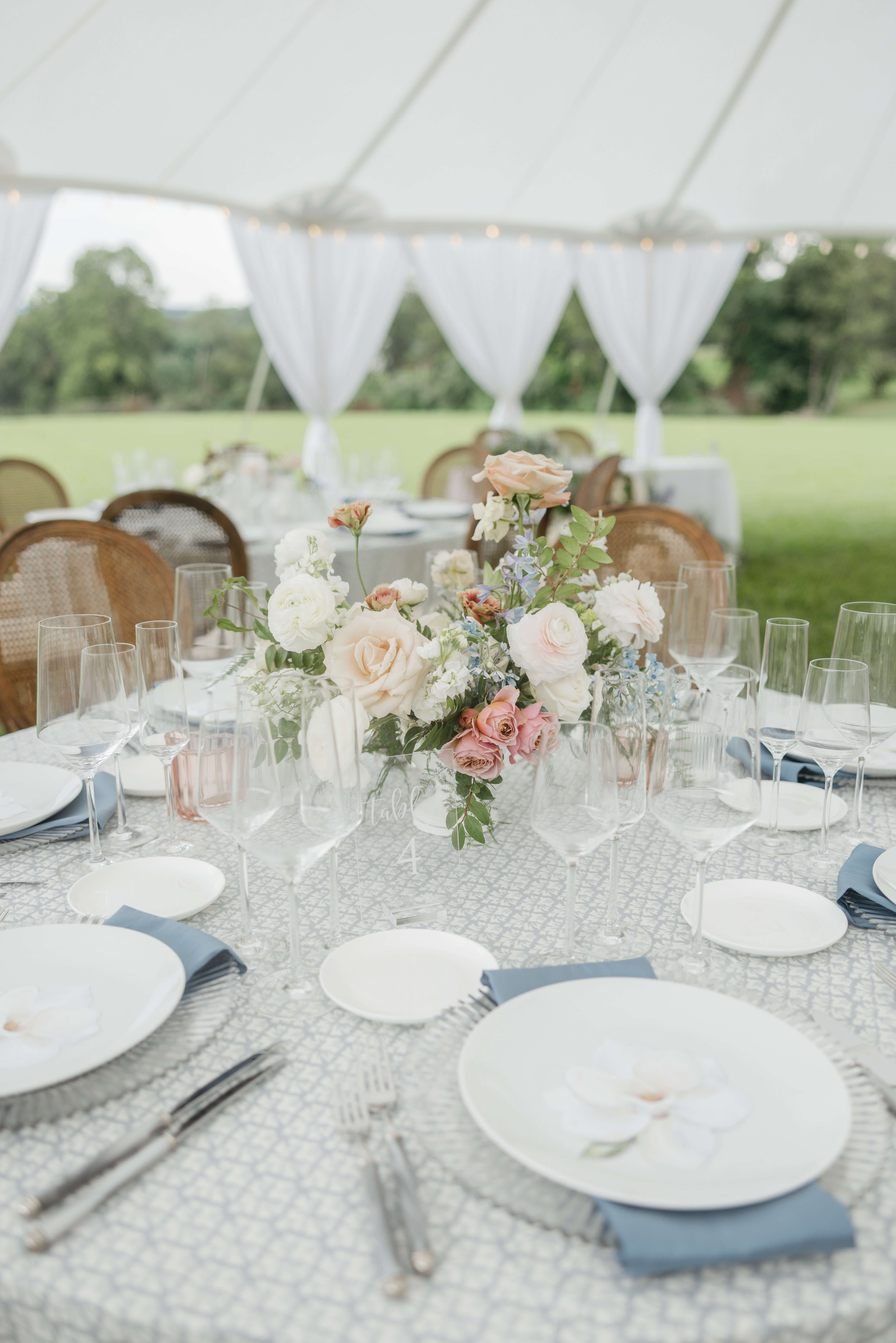 Private Residence Summer Wedding 3 Tables set up outside under large white tent, floral centerpiece with white, pink, peach and light blue flowers