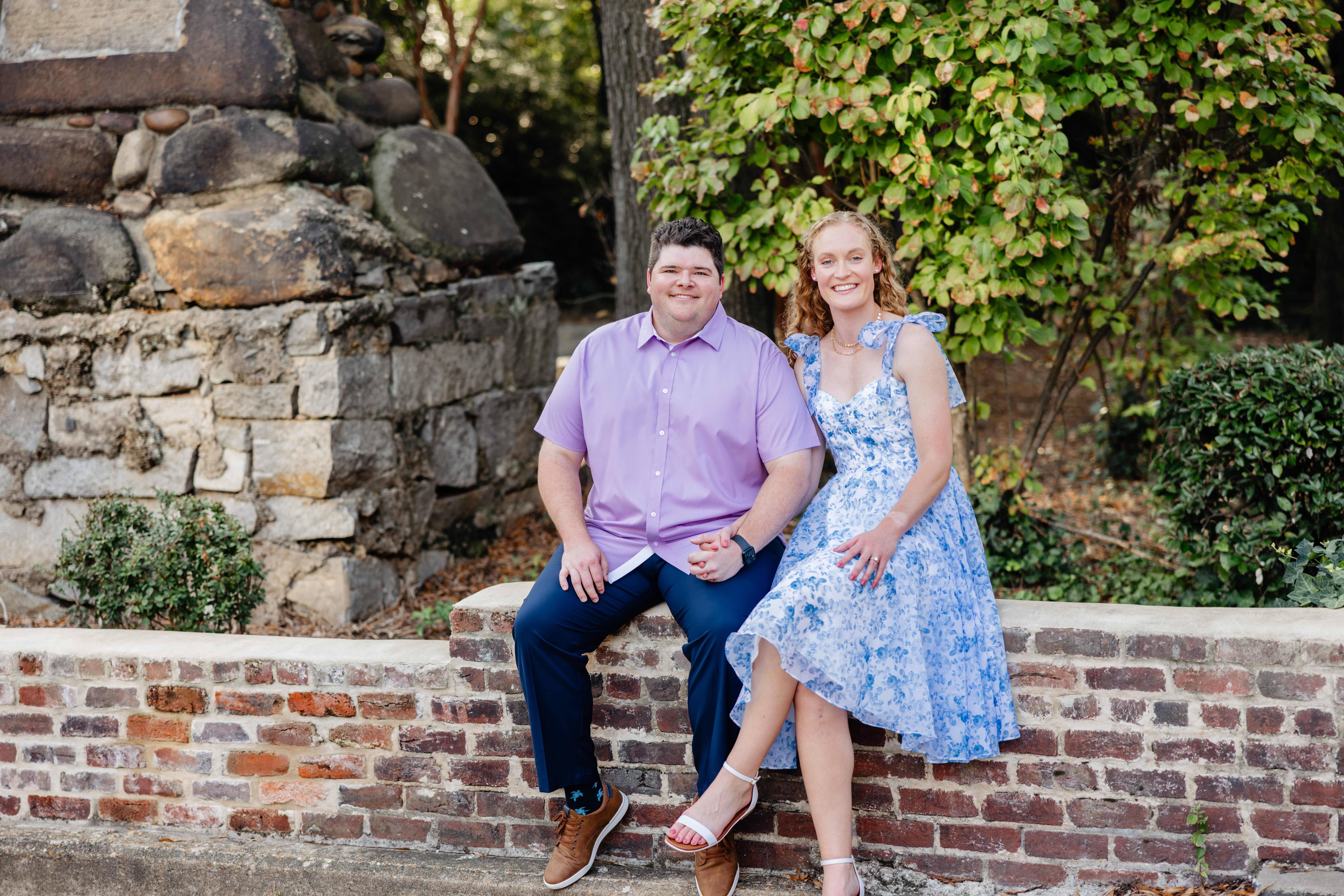 Shockhoe Bottom Fall Engagement Photography 13 Man and woman sit on brick half wall holding hands and smiling at camera