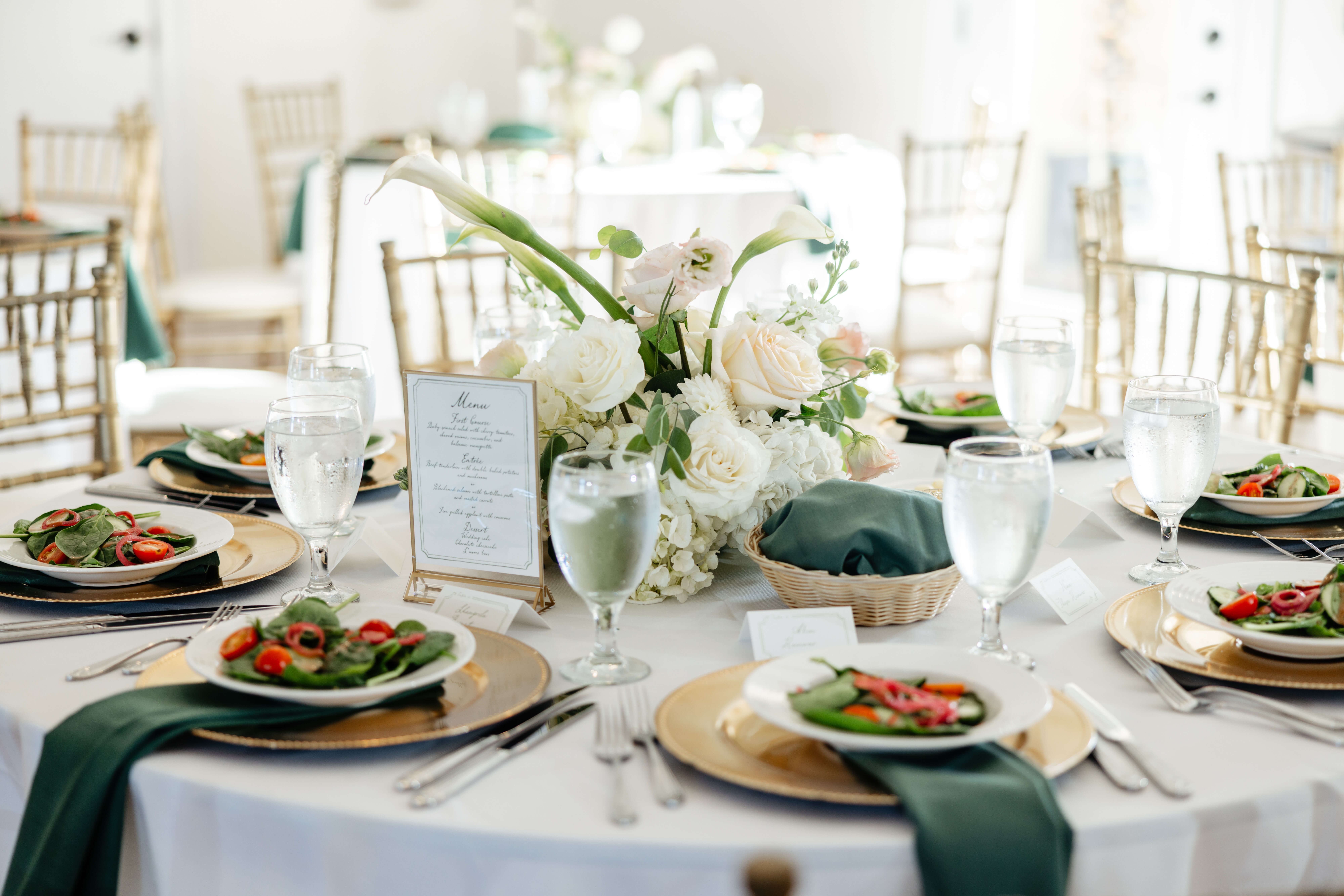 CrossKeys Vineyard Fall Wedding Photography 3 White round table set up with a breautiful white floral arrangements, gold charger plates with white bowls of salad sitting on top of dark green napkins,