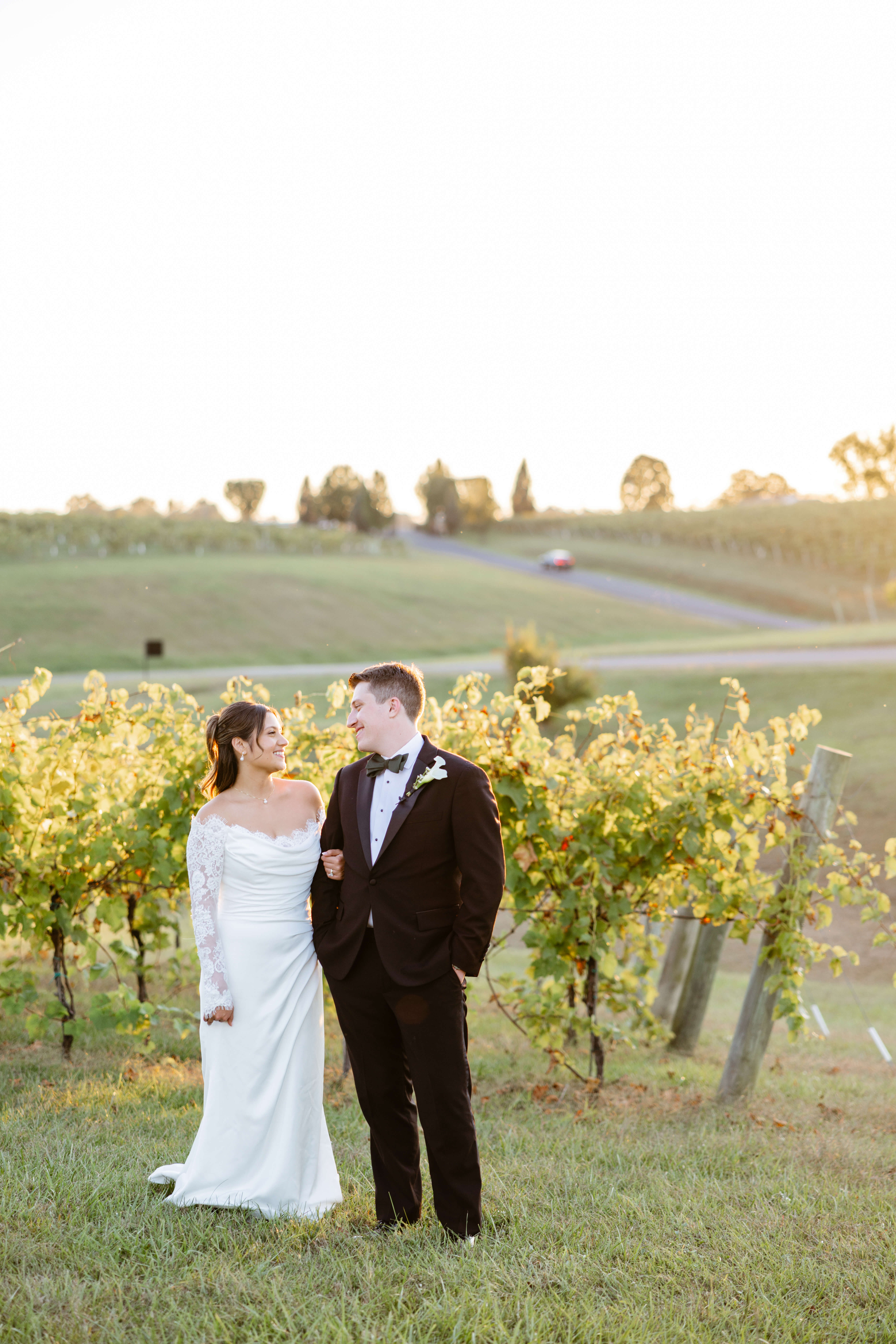 CrossKeys Vineyard Fall Wedding Photography 41 Bride and groom stand in front of vineyard grapevines as they smile at one another