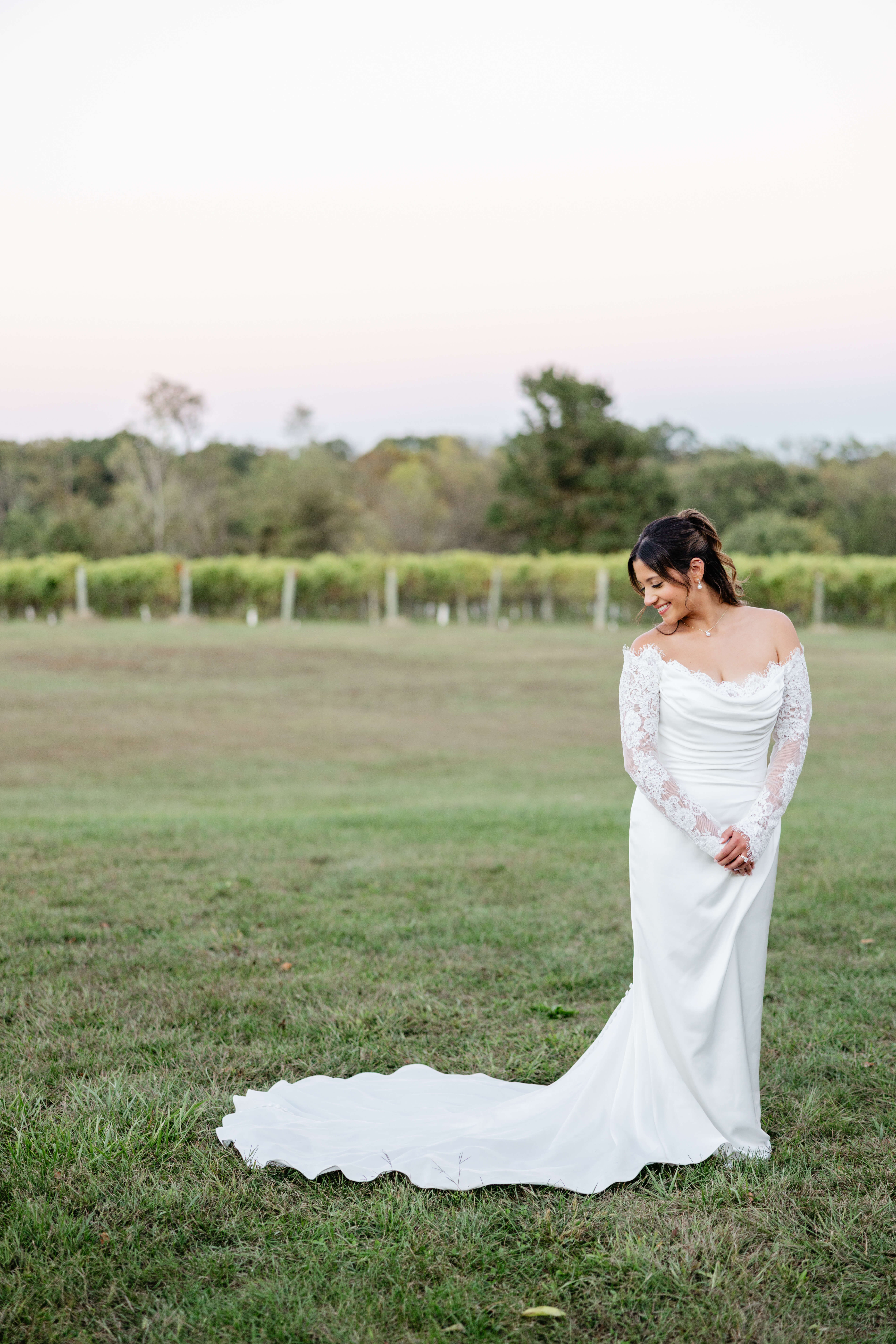 CrossKeys Vineyard Fall Wedding Photography 47 Bride stands in grass by herself smiling back down over her shoulder at her dress train