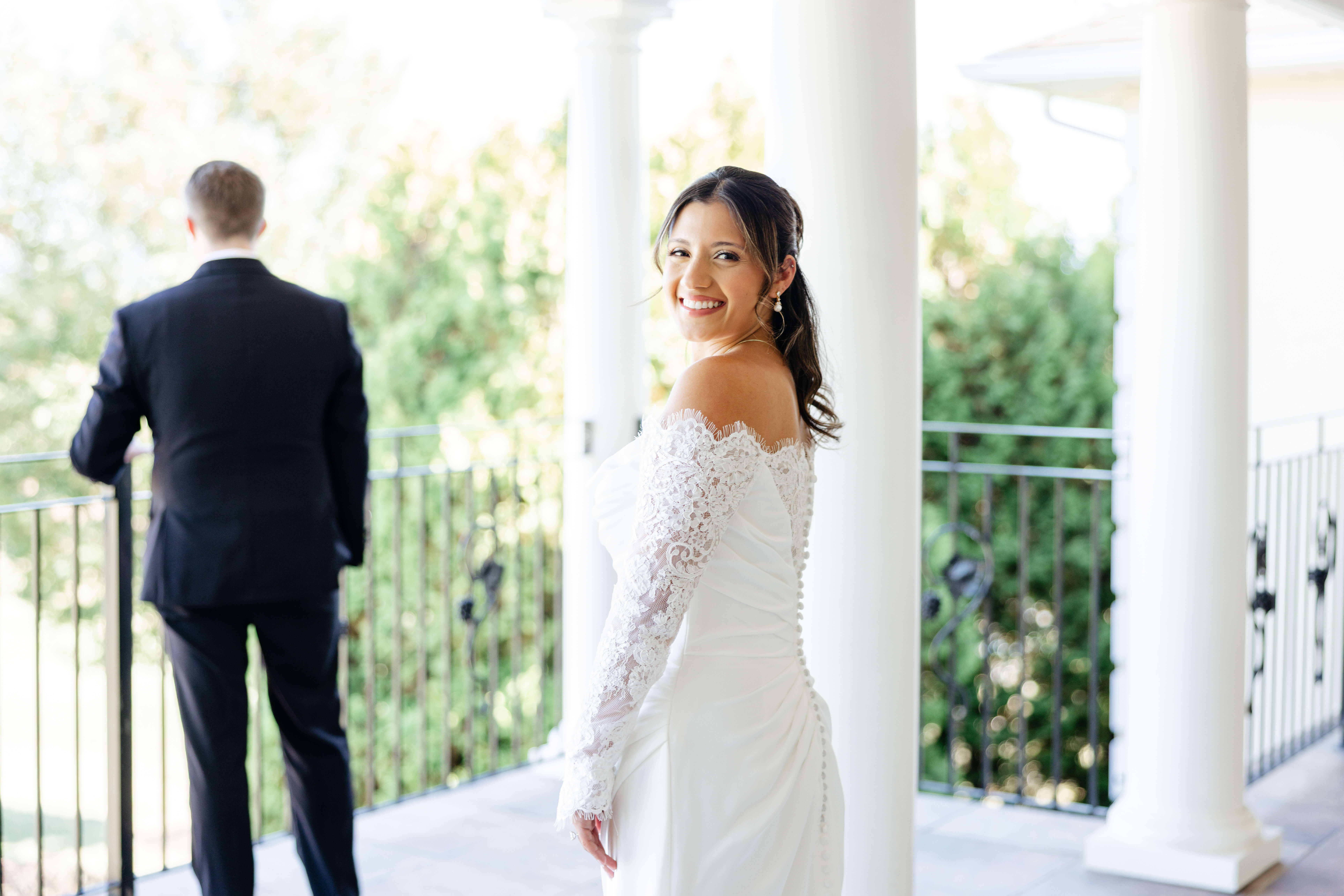 CrossKeys Vineyard Fall Wedding Photography 11 Bride smiling over her shoulder at camera as groom stands in front of her with his back turned to her right before their first look