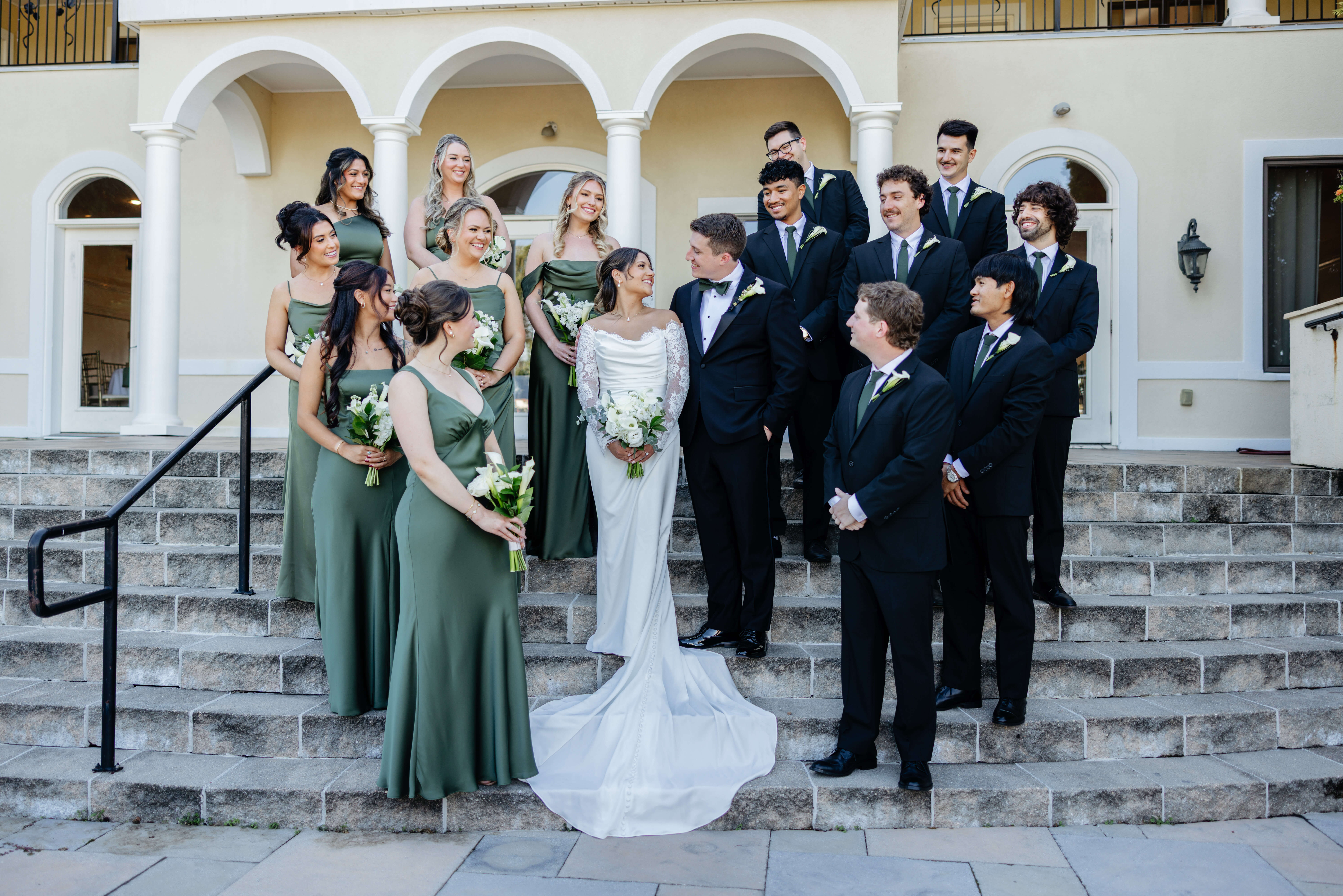 CrossKeys Vineyard Fall Wedding Photography 18 Bride and groom stand on staircase outside smiling at one another as their wedding party stands staggared around them smiling at the couple