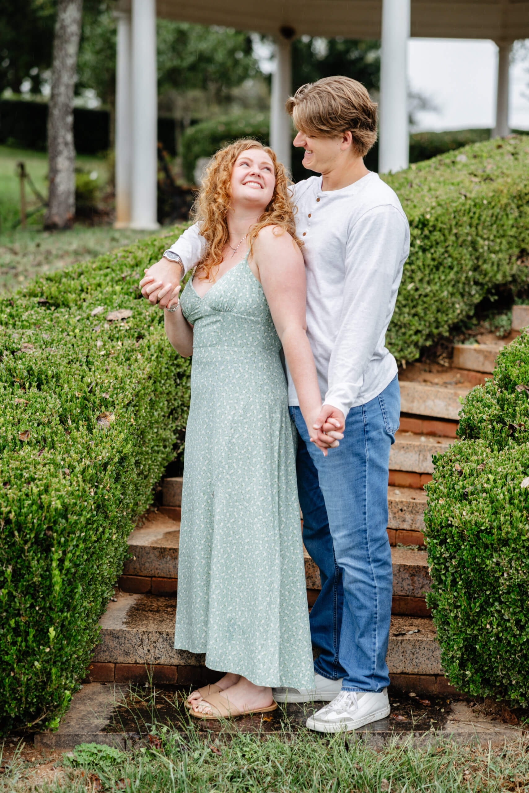 Rassawek Vineyards Fall Engagement Photography 4 Man standing behind his fiancee as she looks up over her shoulder at him smiling as they hold hands