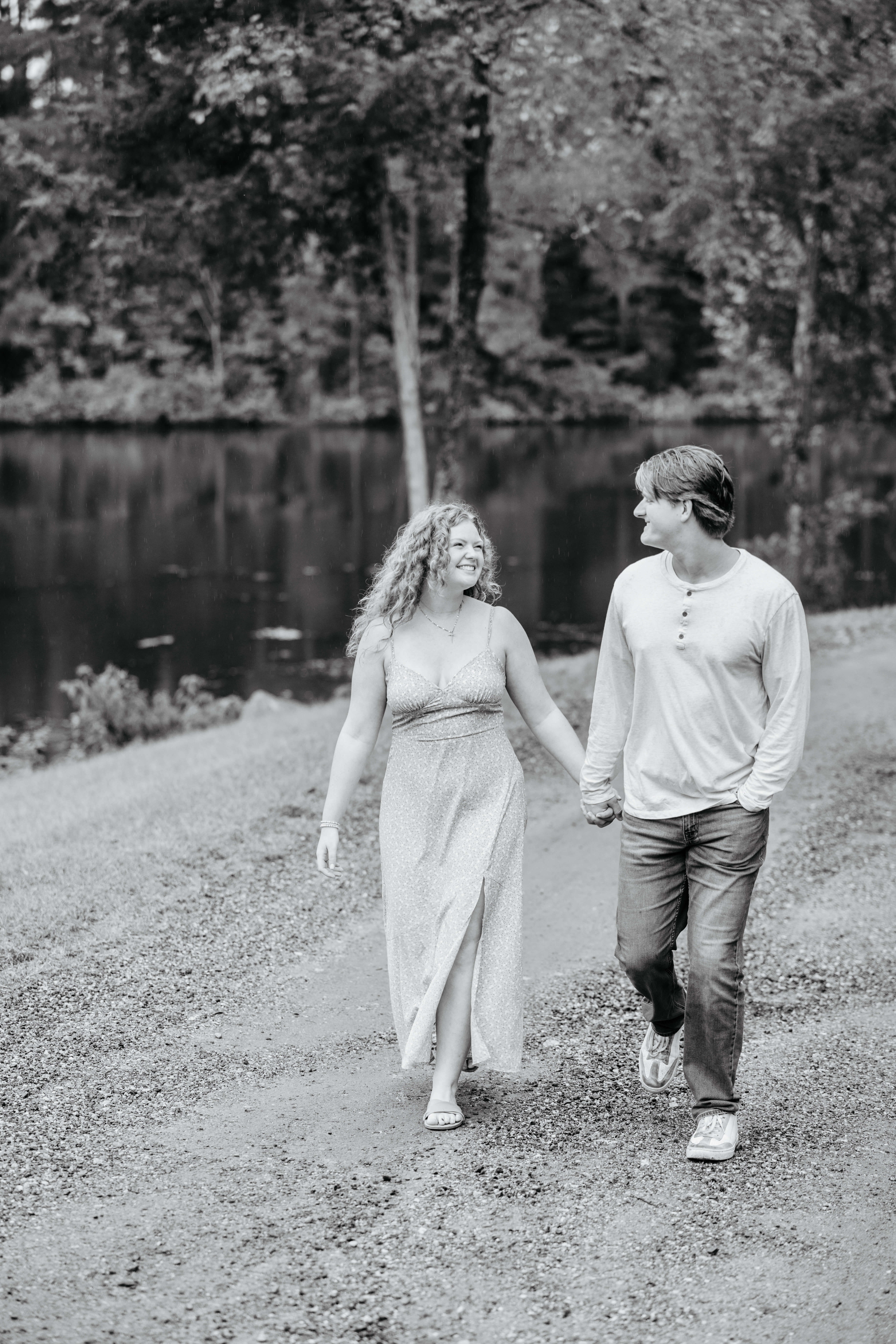Rassawek Vineyards Fall Engagement Photography 10 Black and white photo of engaged couple walking hand in hand next to a pond as they smile at one another