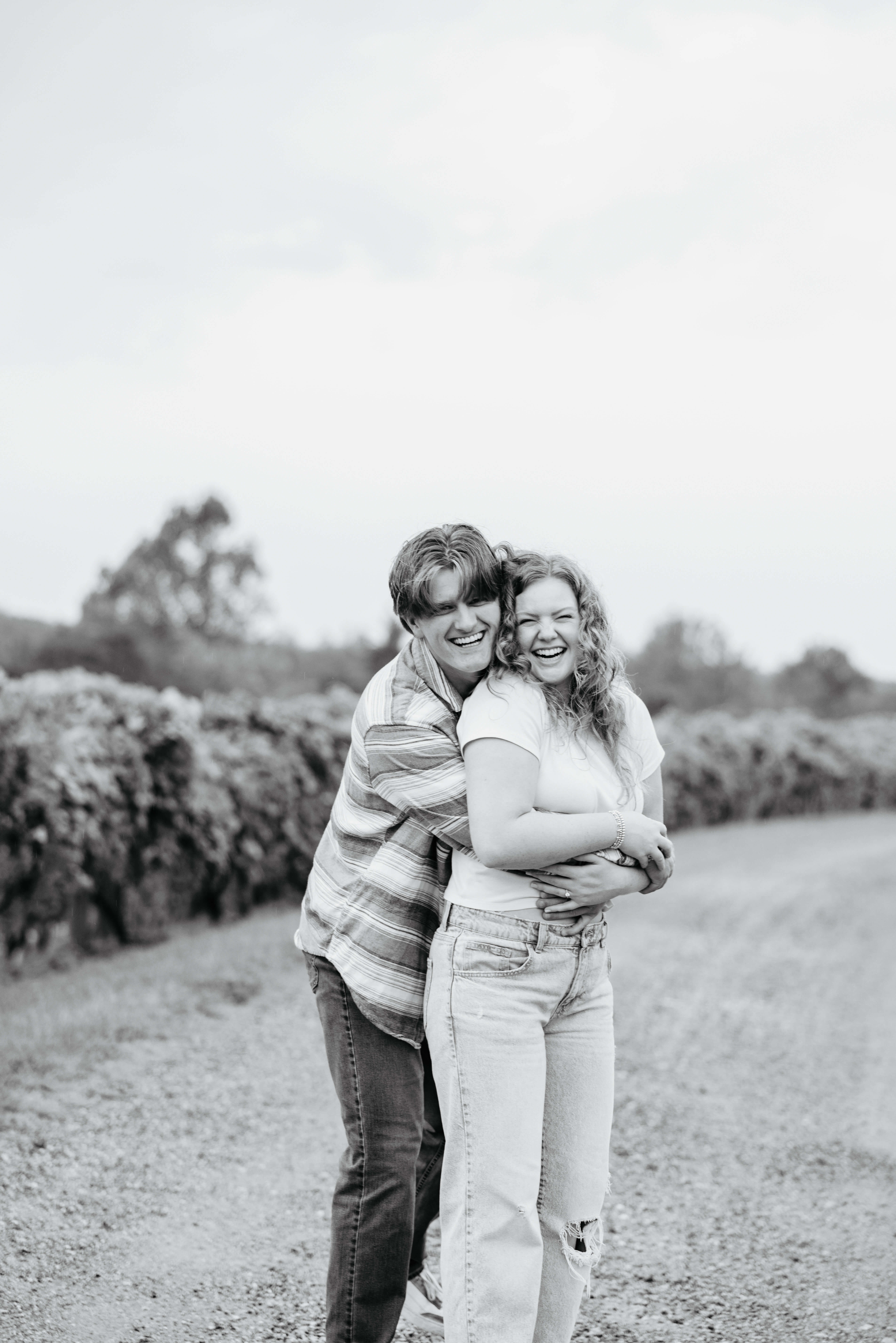 Rassawek Vineyards Fall Engagement Photography 14 Black and white photo of man hugging his fiancee from behind, both laughing