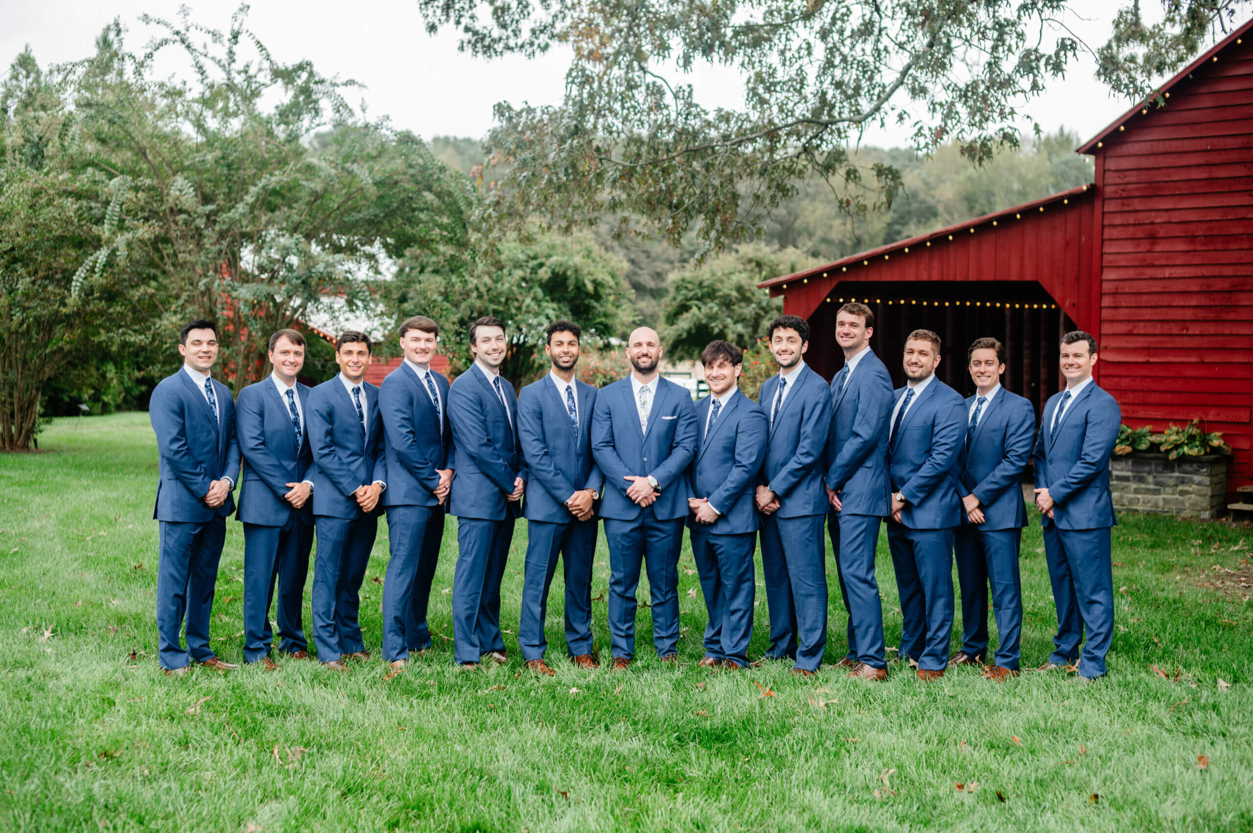 Barns of Kanak October Wedding 7 Groom and his twelve groomsmen standing outside in matching blue suits, red barn on background