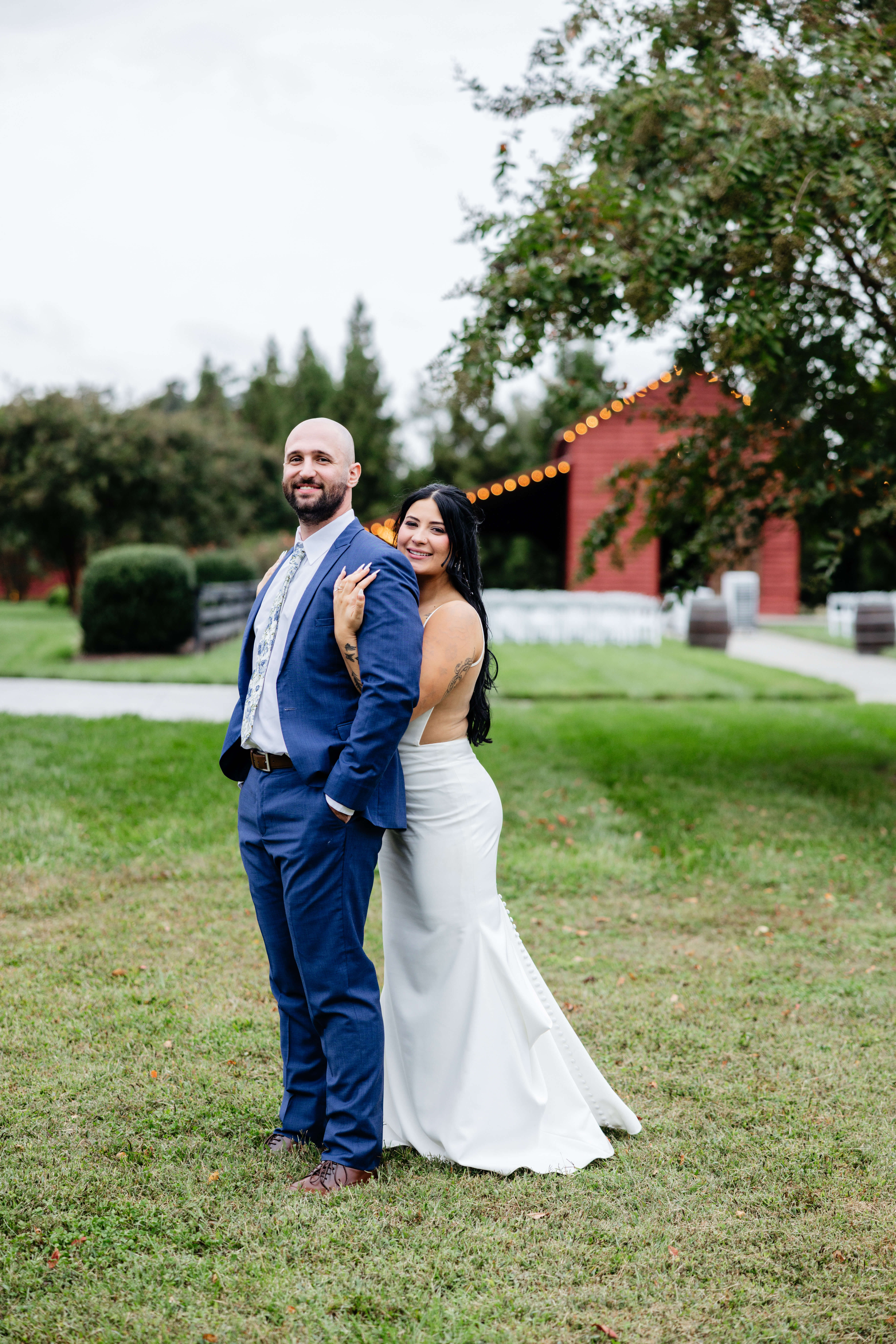 Barns of Kanak October Wedding 42 Bride hugging groom from behind as they both smile at camera, red barn in background