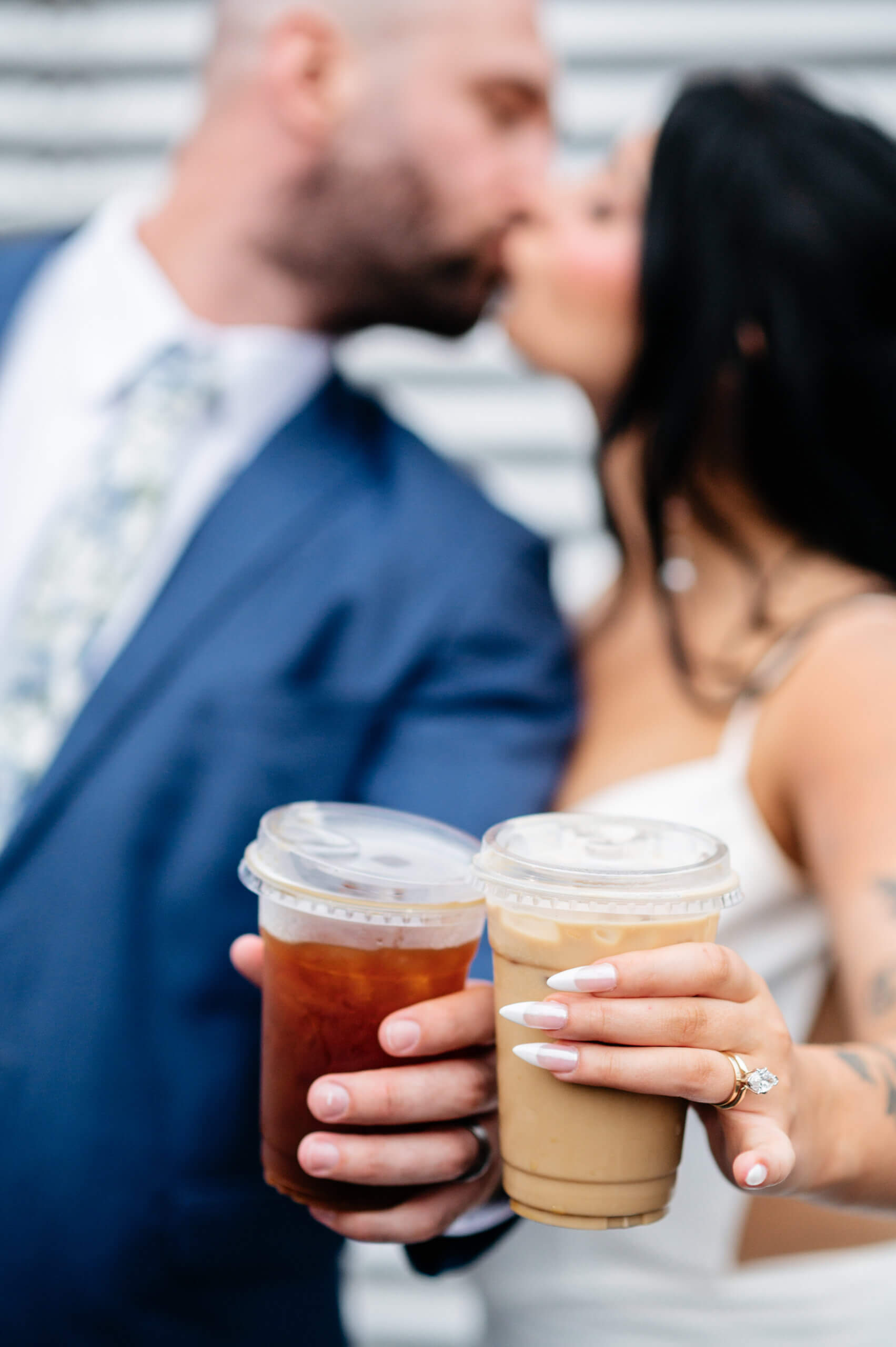 Barns of Kanak October Wedding 46 Bride and groom holding out their iced coffee drinks, bride's ring in view as couple shares a kiss in background of photo