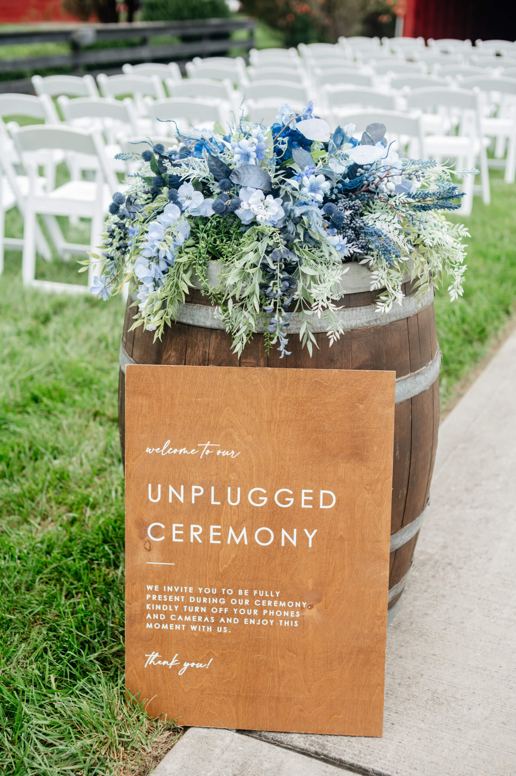 Barns of Kanak October Wedding 12 Wooden sign about unplugged ceremony, leans against a large wooden barrel with beautiful blue floral arrangement on top of it