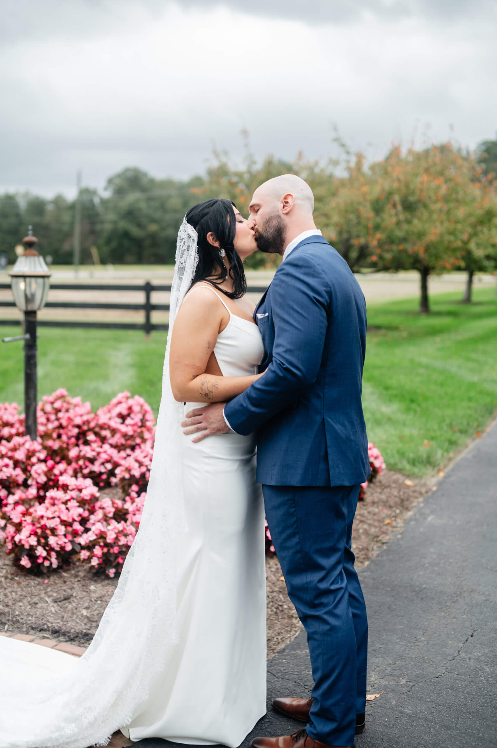 Barns of Kanak October Wedding 15 Bride and groom share a kiss outside, pink flowers on ground behind them and trees off in distance