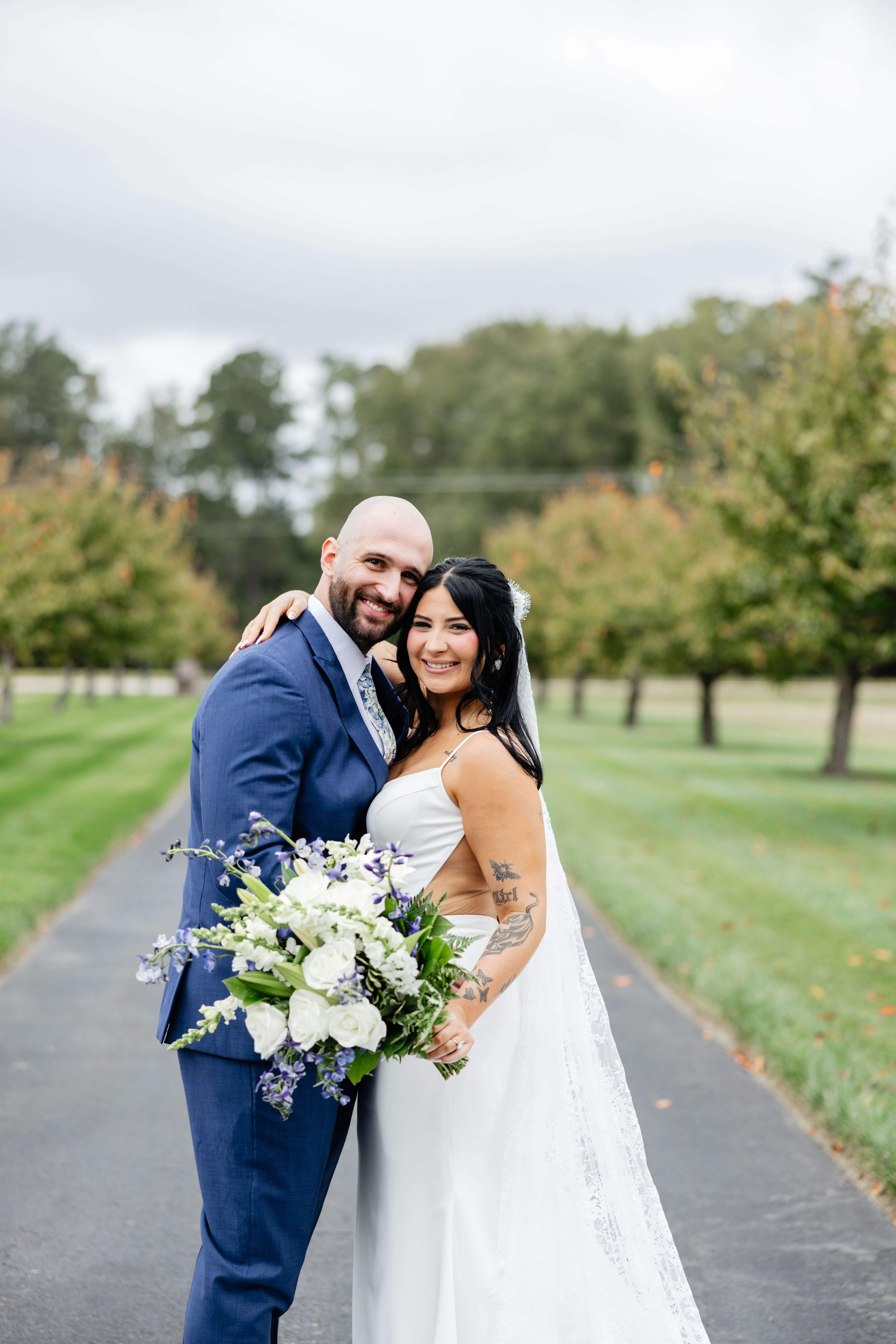 Barns of Kanak October Wedding 16 Bride and groom facing one another, heads turned to smile at camera, bride holds large bouquet of white flowers with small blue/purple accent flowers