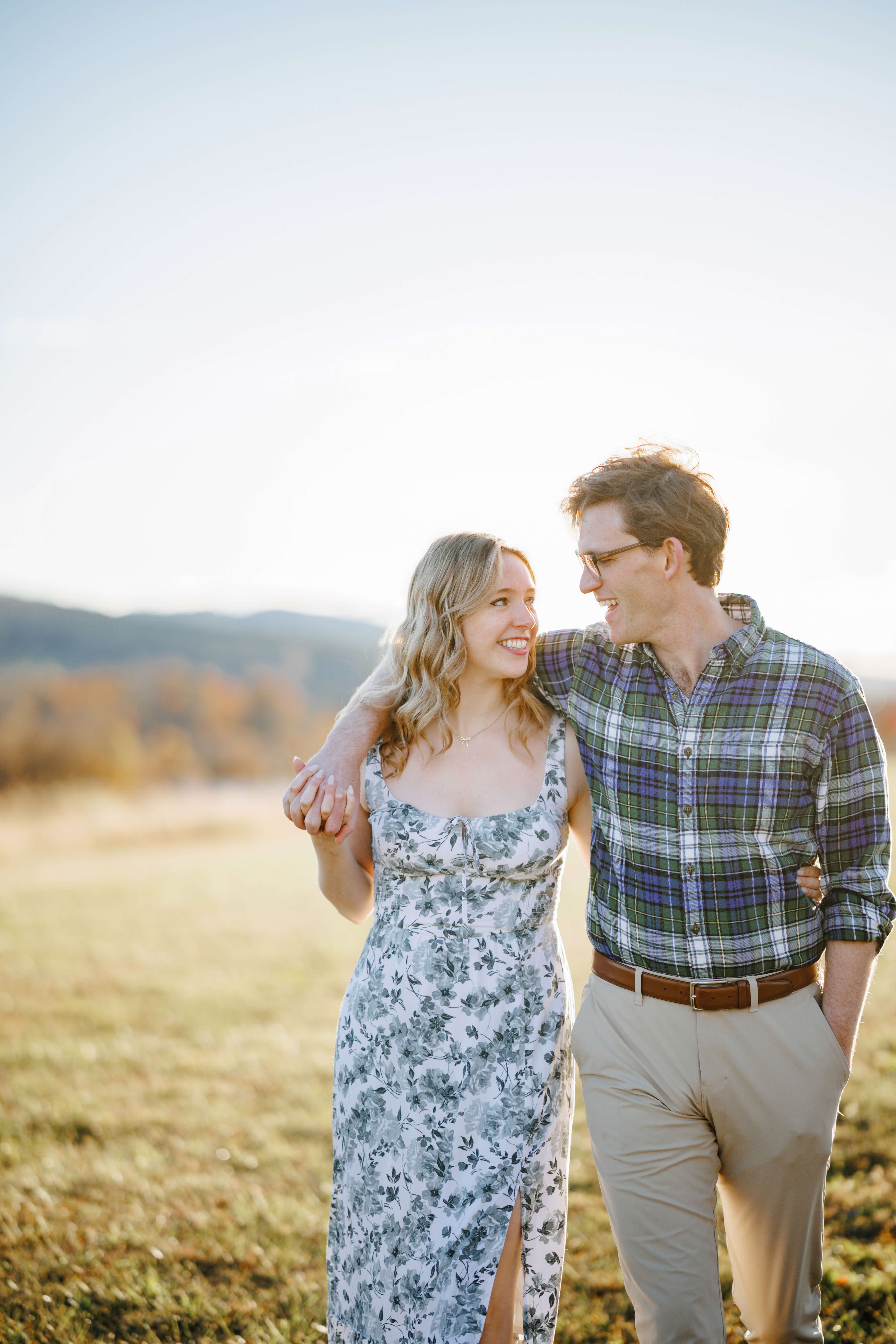 Market at Grelen Fall Engagement Photography 16 Man and woman walking togther, man has his arm around his fiancee as she interlocks her fingers with his and they smile at one another