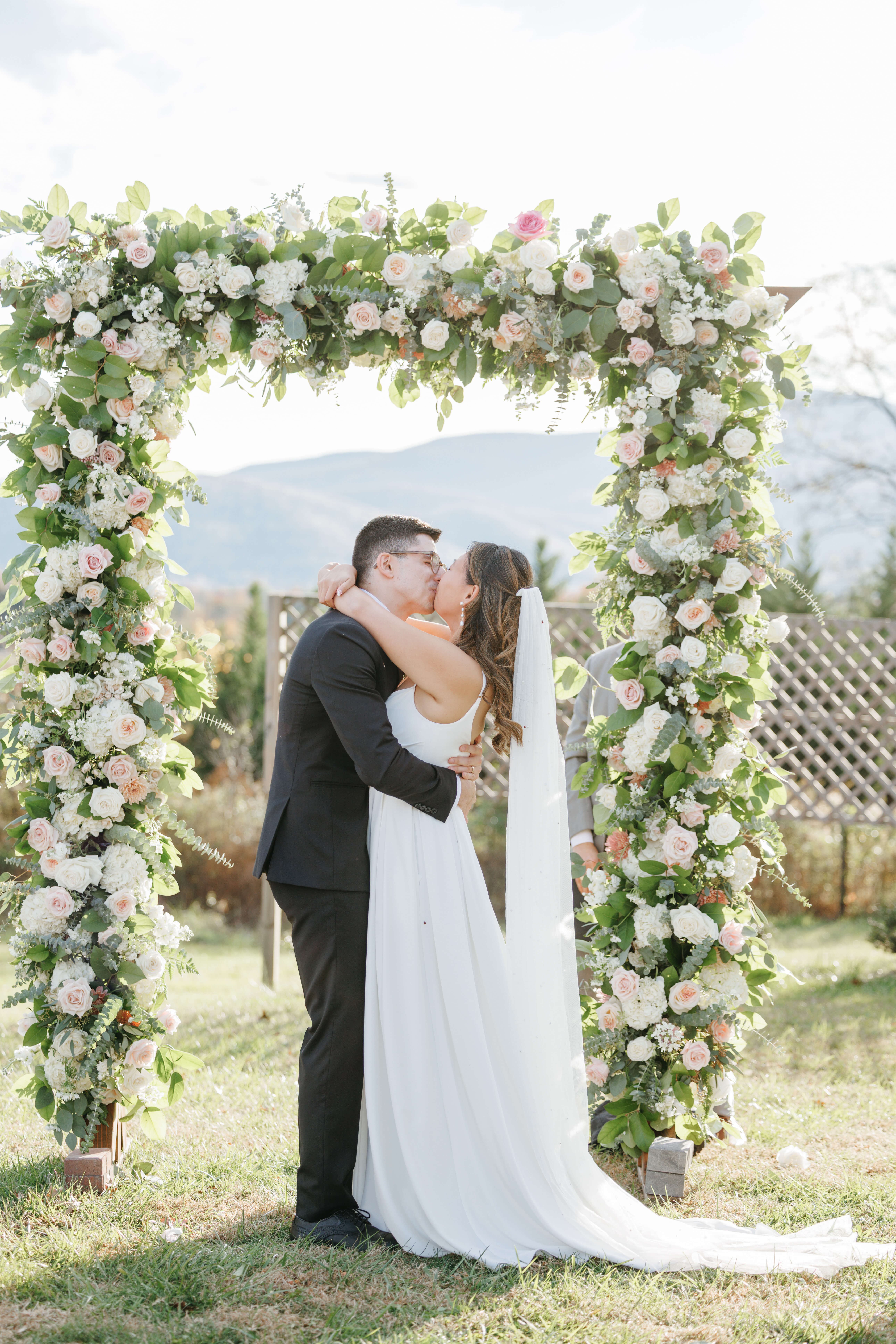 Valley Road Vineyard Fall Wedding 29 Bride and groom share first kiss as husband and wife in front of beautiful rectangle arch covered in greenery and pink florals