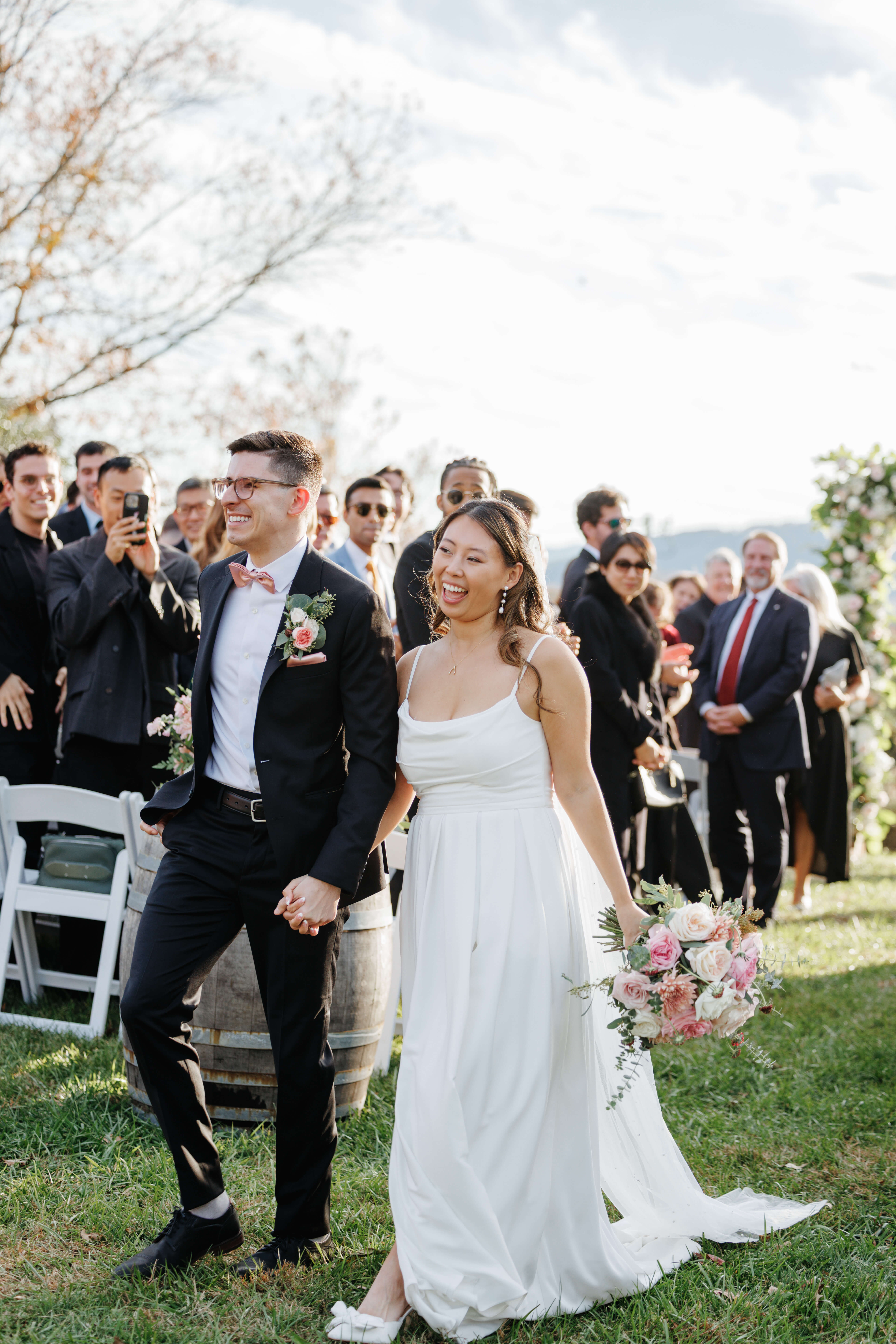 Valley Road Vineyard Fall Wedding 30 Bride and groom walk back up aisle smiling as guests stand at their seats ,smiling and taking photos