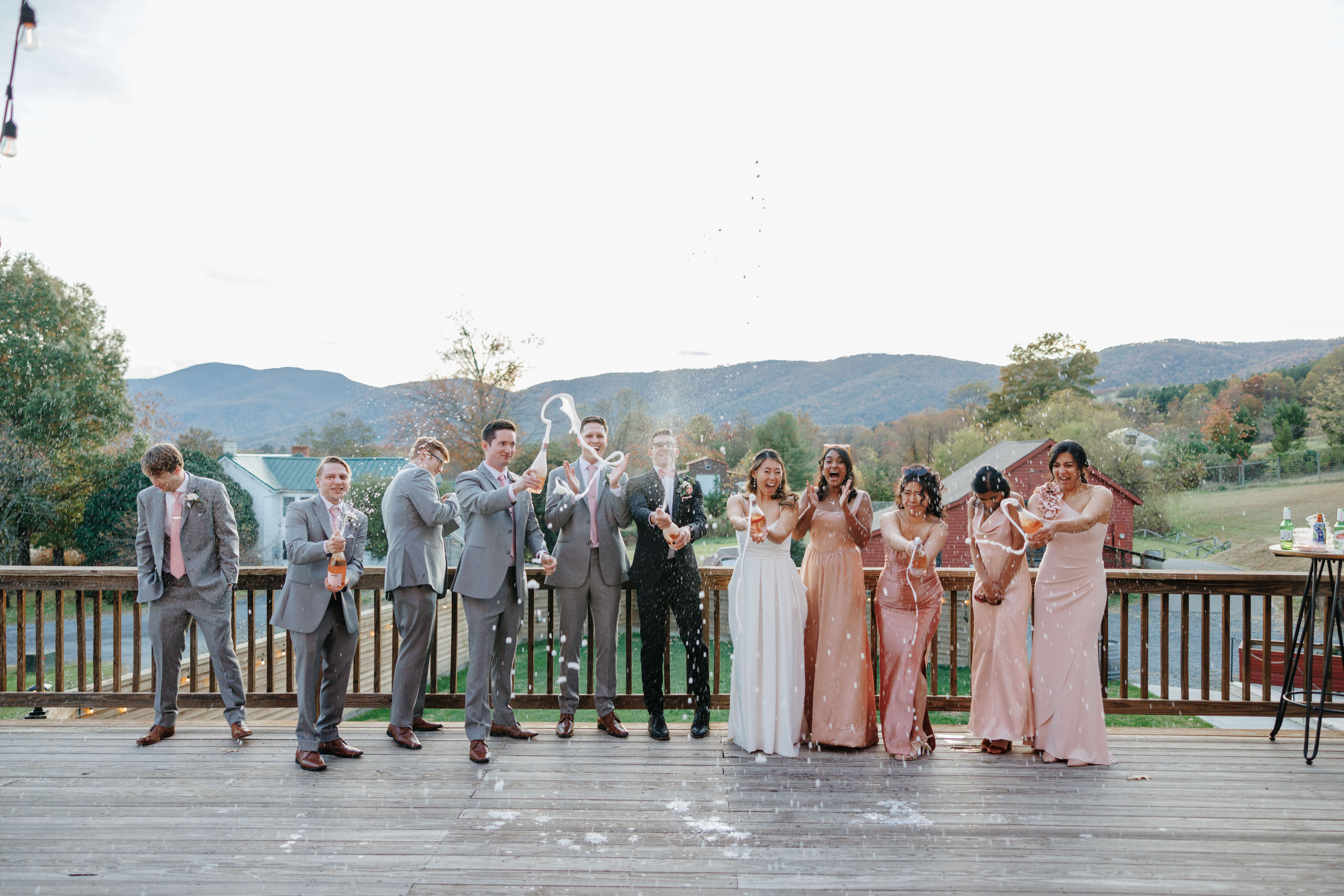 Valley Road Vineyard Fall Wedding 39 Bride and groom popping champagne with their wedding party on a balcony outside at valley road vineyard