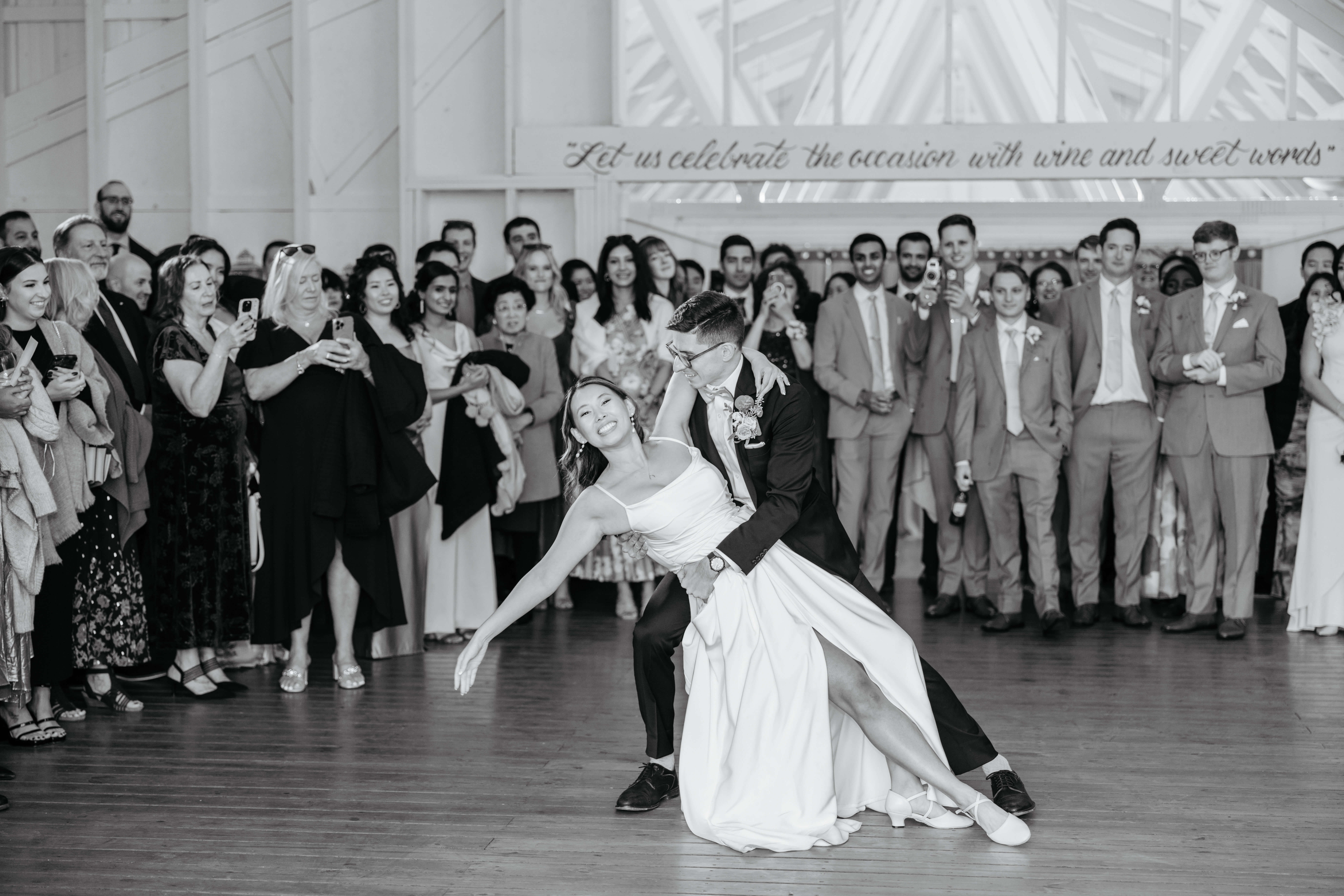 Valley Road Vineyard Fall Wedding 44 Black and white photo of bride dipped, arm out smiling at camera during the first dance as guests watch and take photos
