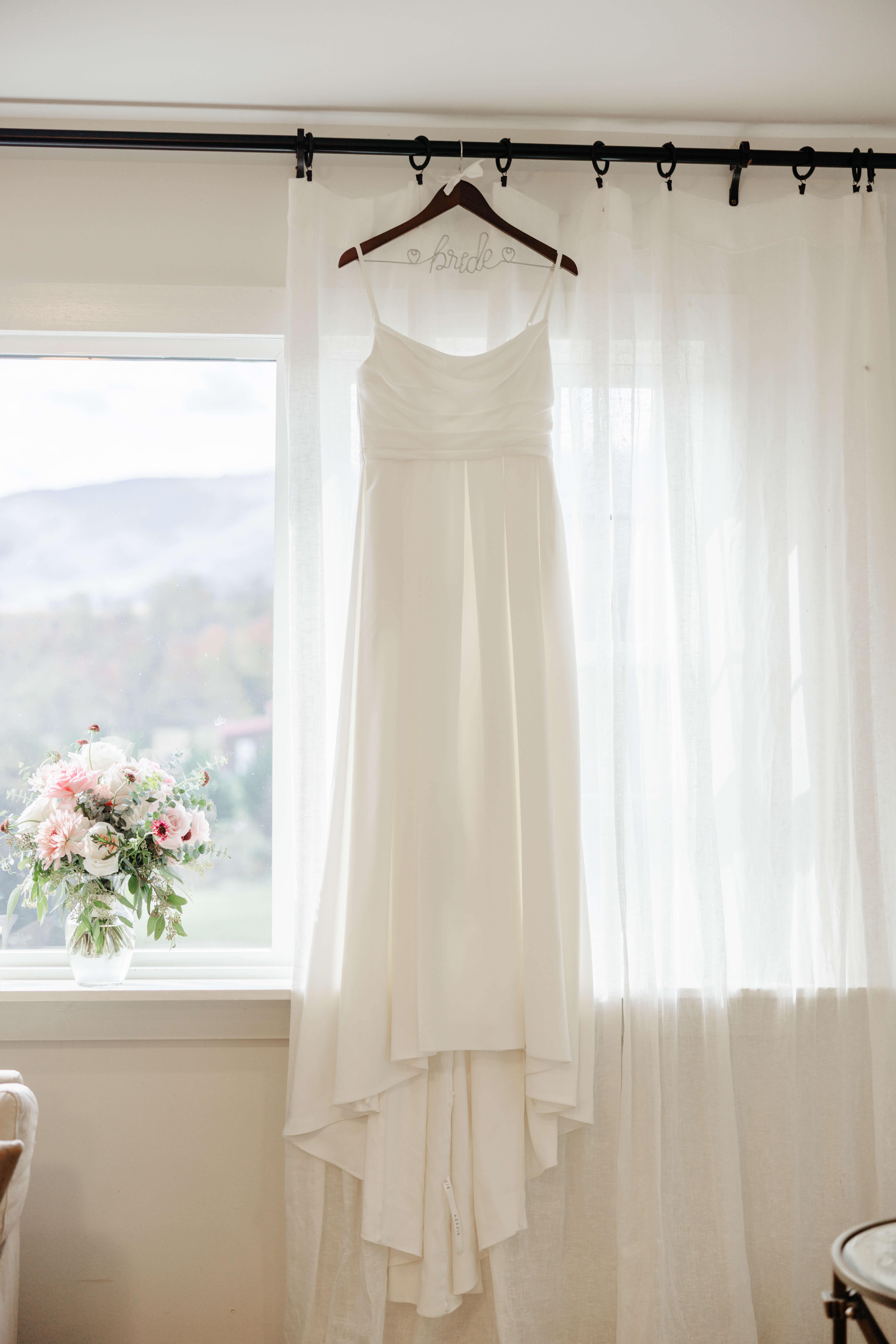 Valley Road Vineyard Fall Wedding 3 White wedding dress hangs in front of window with mountain views, bride's bouquet sits in clear vase on the window sil