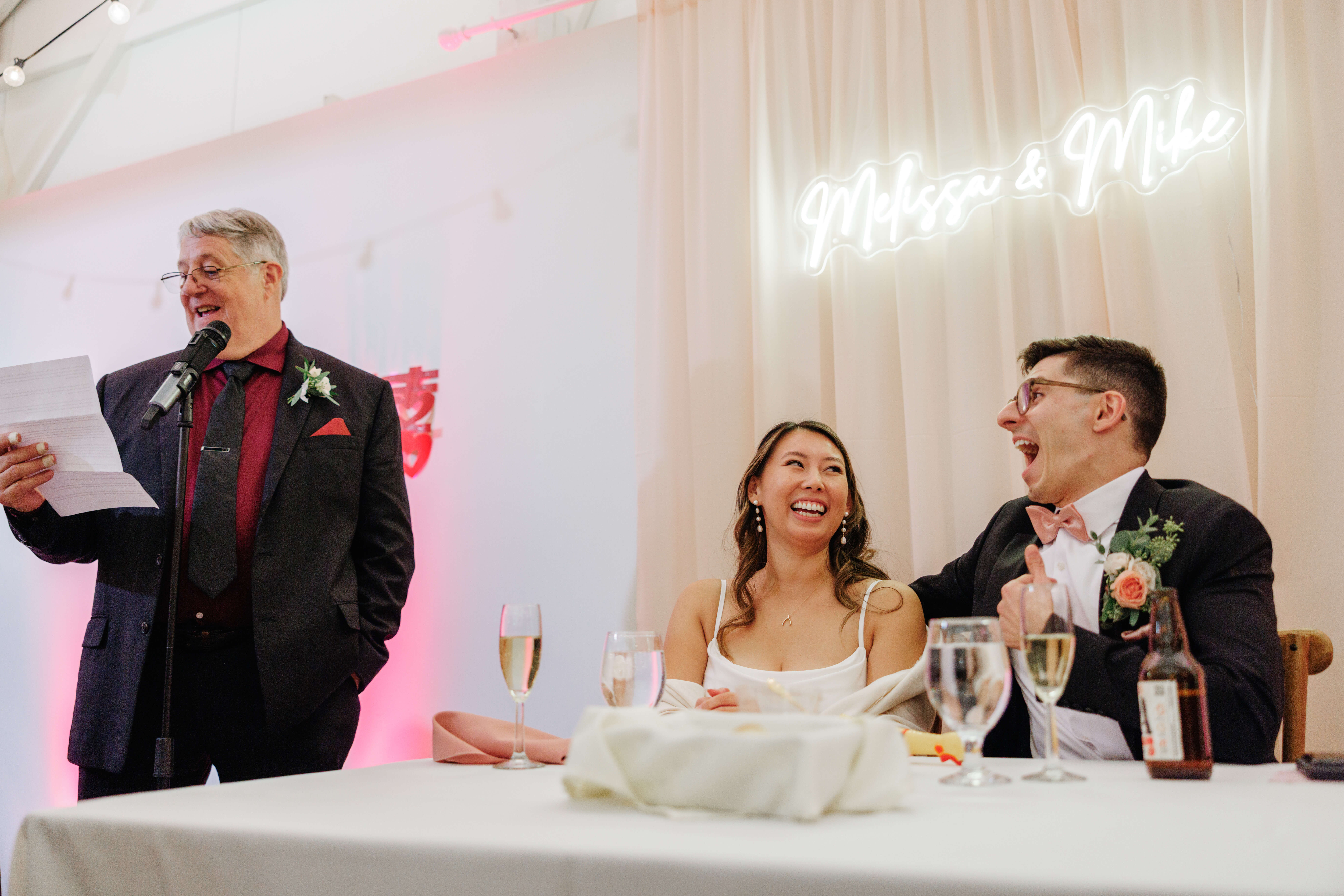 Valley Road Vineyard Fall Wedding 45 Groom's dad giving speech as bride and groom sit at sweetheart table laughing