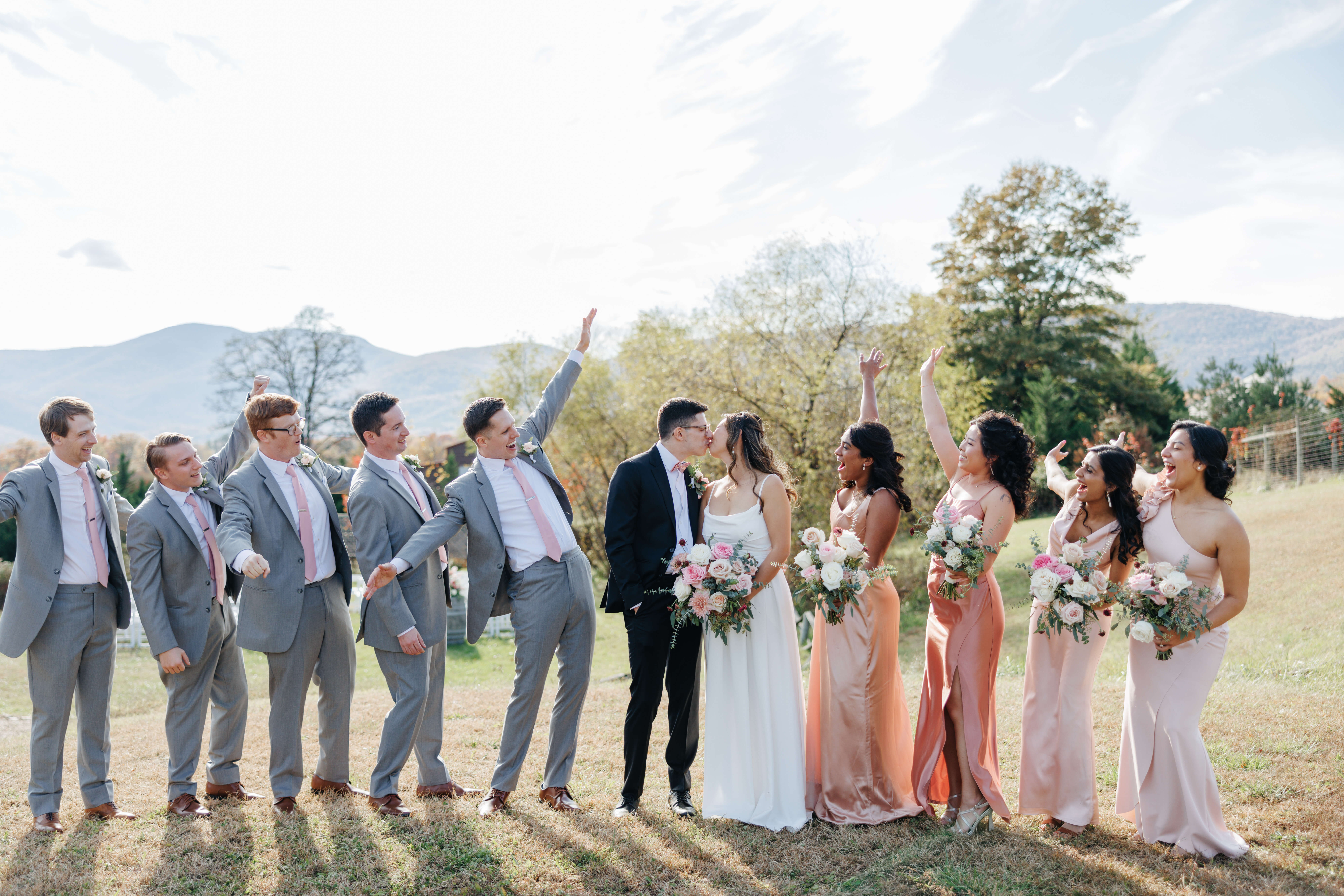 Valley Road Vineyard Fall Wedding 13 Bride and groom share a kiss as their wedding party stands on either side of them cheering and smiling at couple