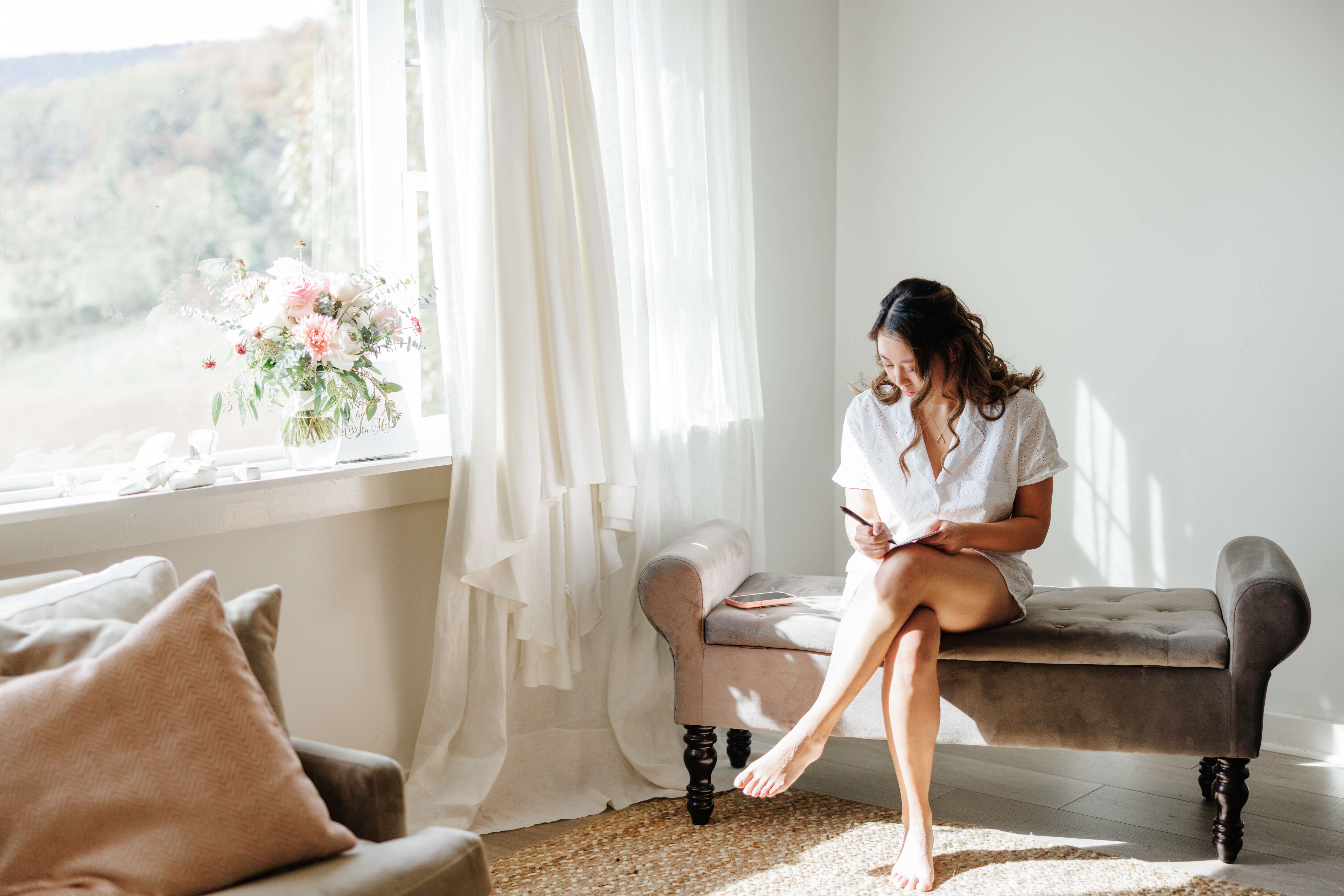 Valley Road Vineyard Fall Wedding 2 Bride sits in white pjs writing a note, next to her are her wedding dress and bouquet
