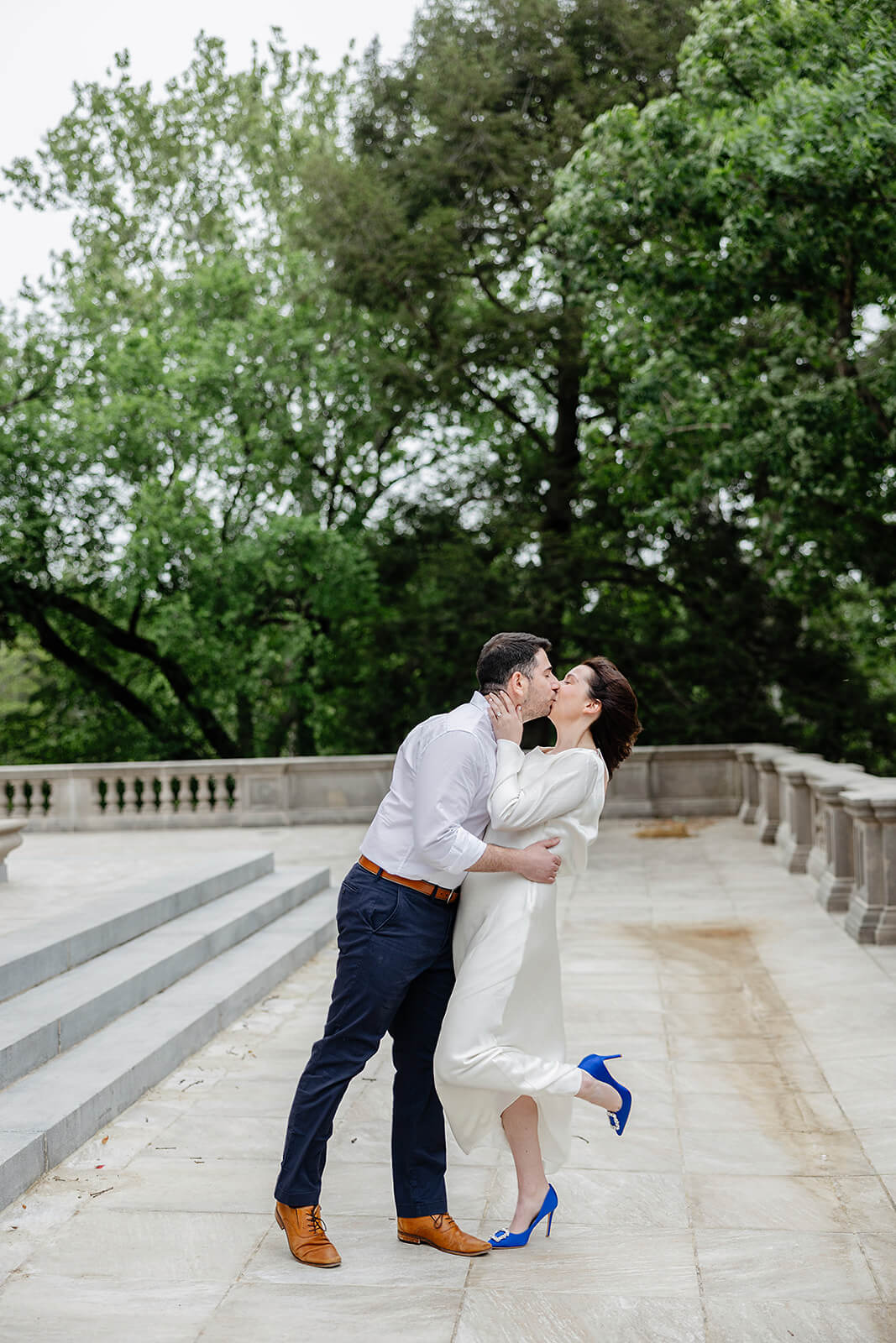 Carillon War Memorial Engagement 4 man kissing and dipping a woman on stone patio with stone railings. there are tall trees behind them and she in wearing vibrant blue shoes with diamond buckles