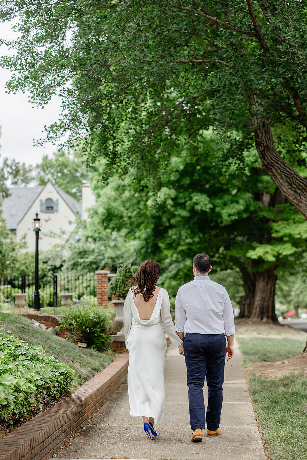 Carillon War Memorial Engagement 11 couple holding hands and walking away from the camera. they are walking done a sidewalk and there is lush greenery and trees around them