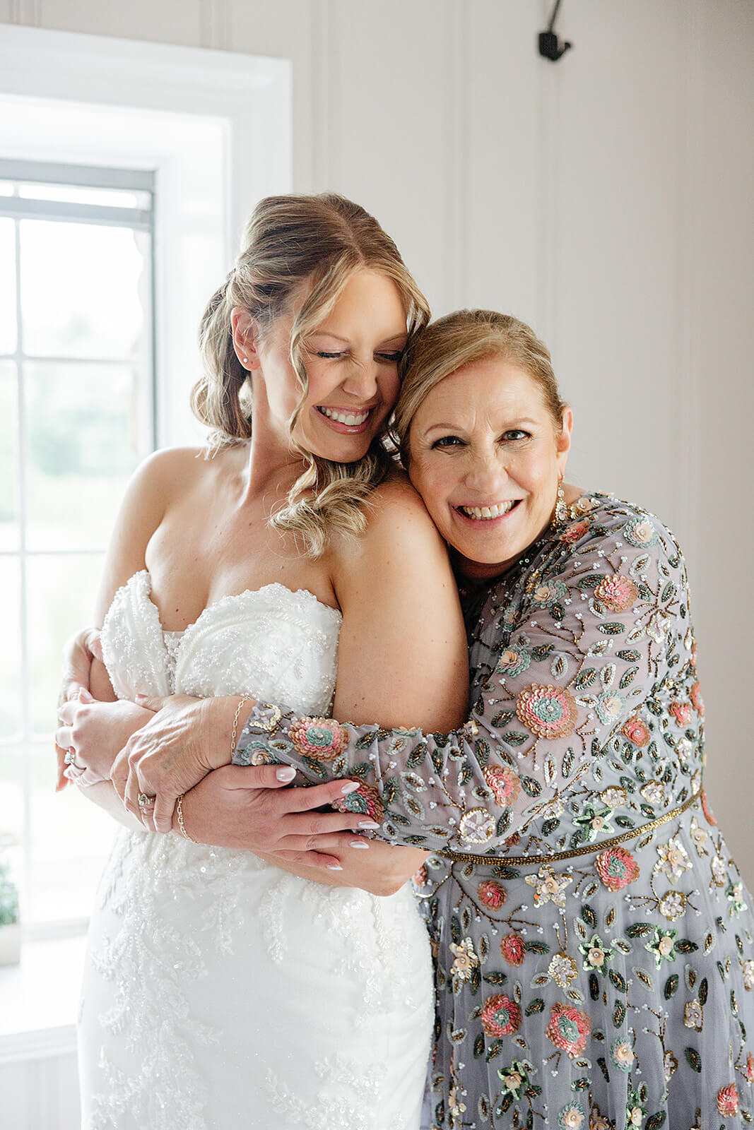 Poplar Springs Manor Spring Wedding Photography 3 bride in her dress being hugged by her mom, who is wearing a grey dress covered in flowers