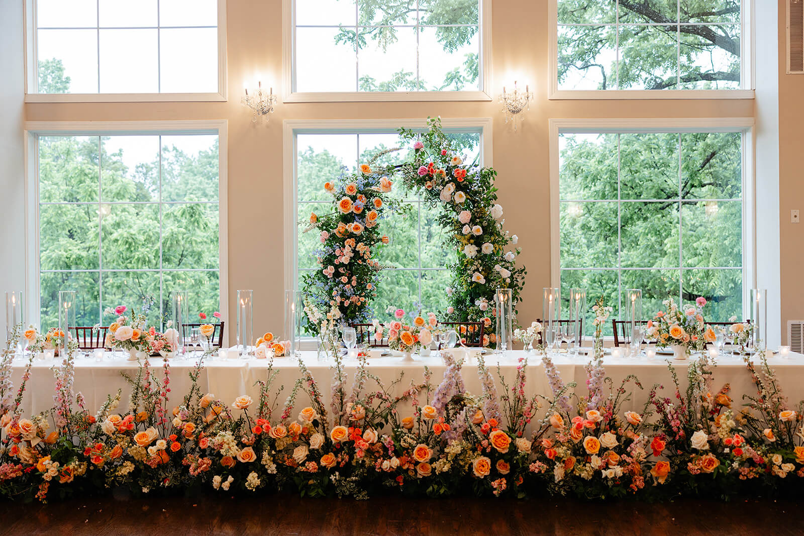 Poplar Springs Manor Spring Wedding Photography 30 long reception table with floral arch behind it and many long floral arrangements on the floor in front of it