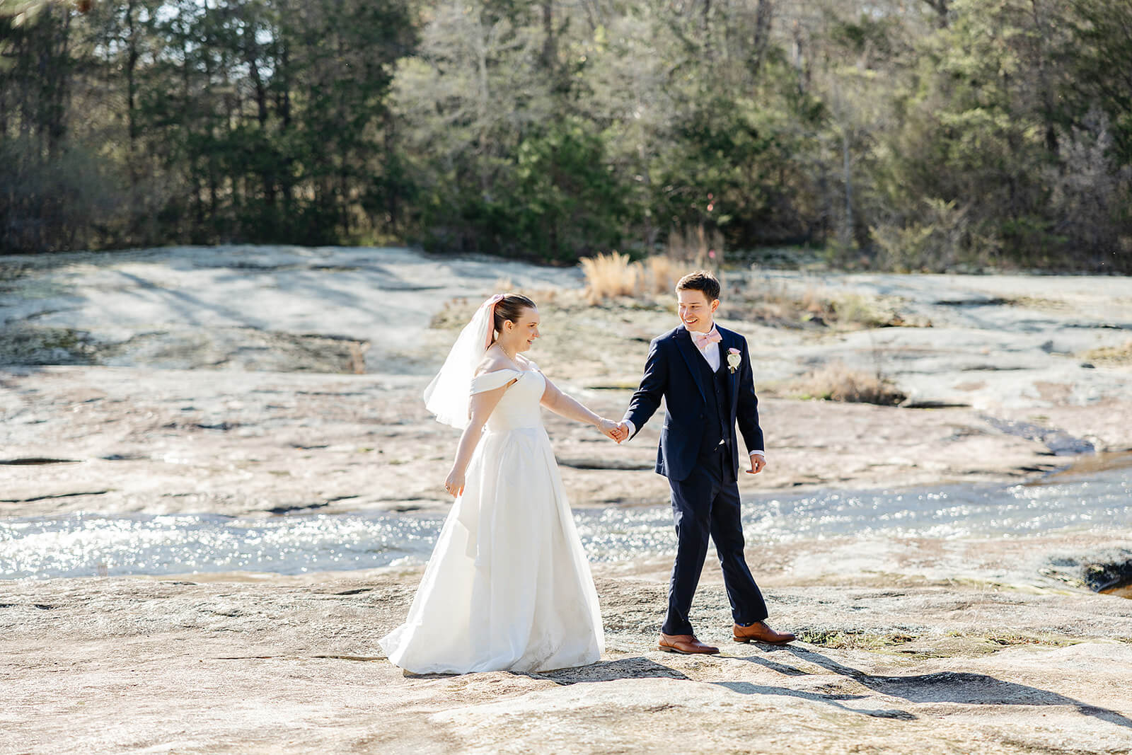 The Mill at Fine Creek Spring Wedding Photography in Powhatan 32 bride and groom holding hands on walking on large, flat rocks in a river