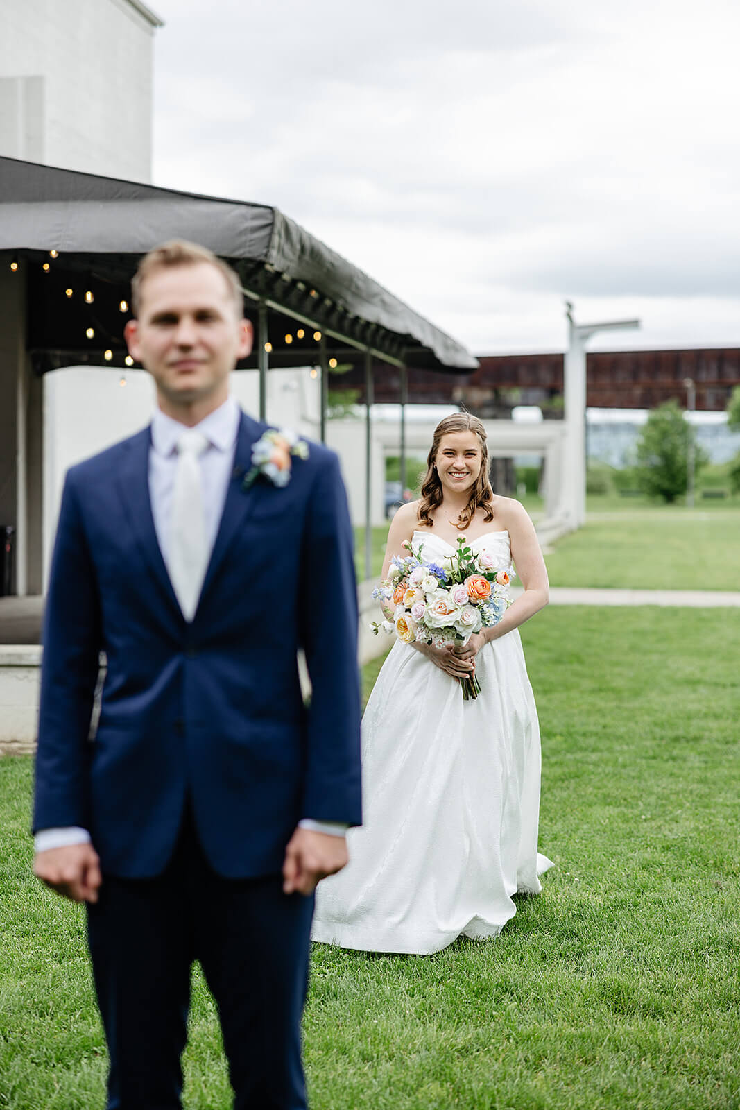 Allegheny RiverTrail Park Spring Wedding Photography 8 bride walking towards groom, he is turned away from her as she walks across a lawn holding her bouquet
