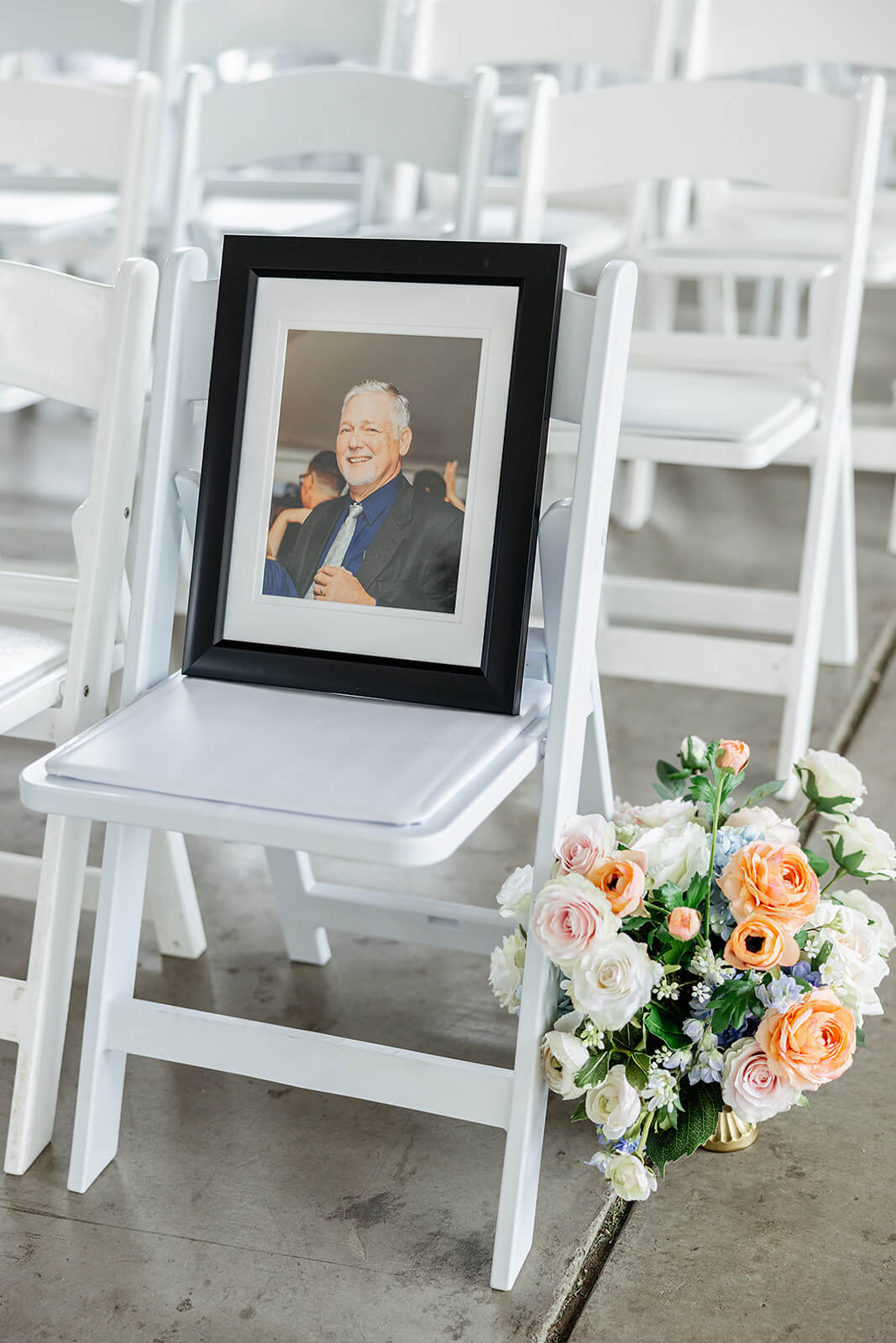 Allegheny RiverTrail Park Spring Wedding Photography 15 white chair with floral arrangement on the ground, there is a picture of a man sitting in the chair