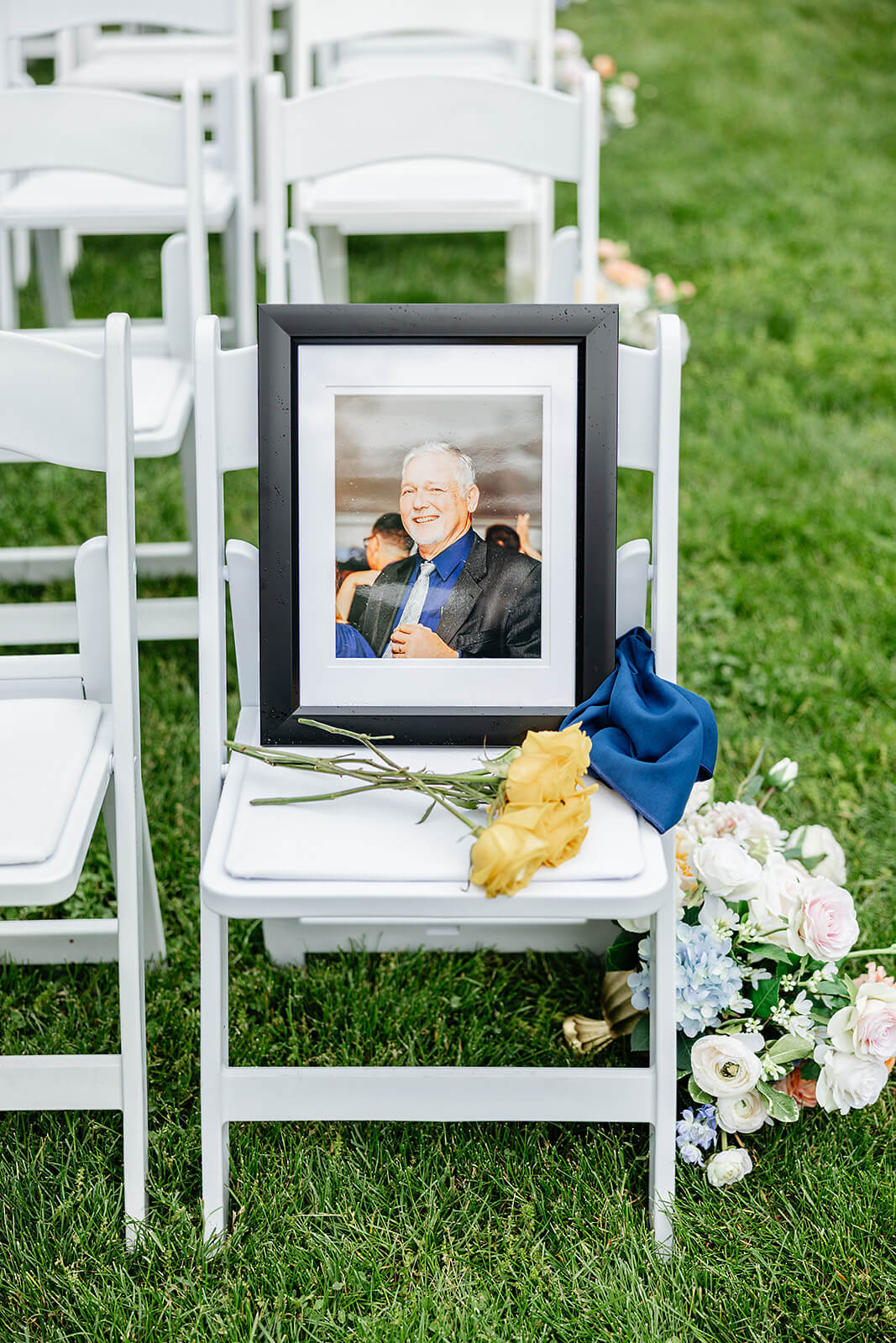Allegheny RiverTrail Park Spring Wedding Photography 18 white chair with floral arrangement on the ground, there is a picture of a man sitting in the chair